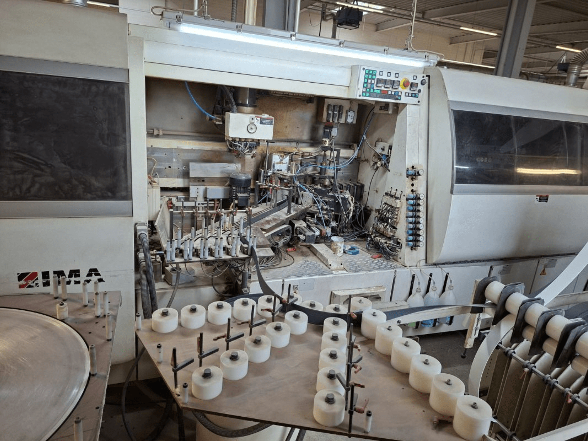 Машини IMA збоку, демонструючи складні механічні компоненти та круглий стіл з білими котушками.