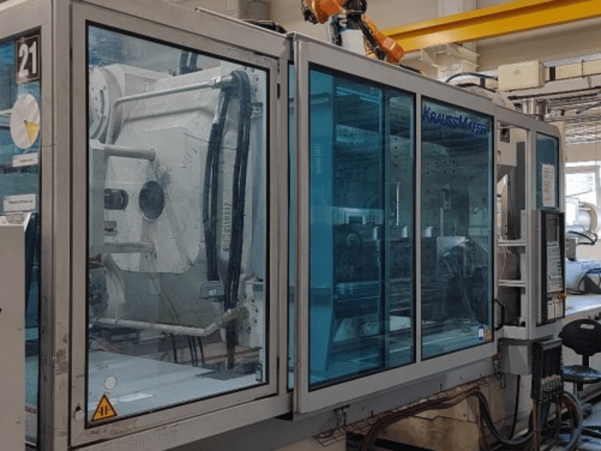 Гідравлічна термопластавтомат Krauss Maffei KM 575-2700 C2, вид збоку, з прозорими захисними панелями та панеллю управління.