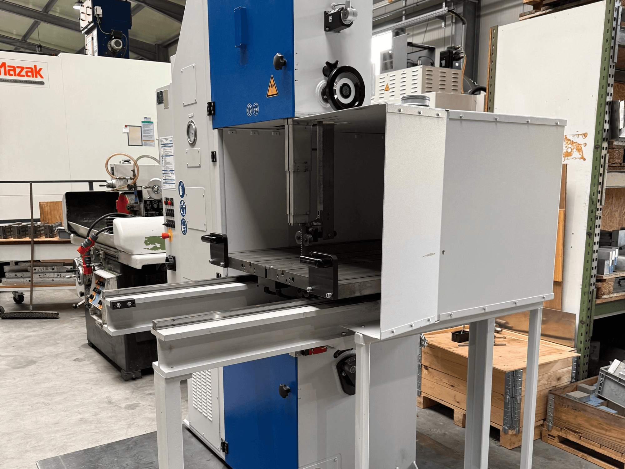 Промисловий верстат Mazak, вид спереду, з синьою панеллю керування, металевим столом і попередженнями про безпеку.