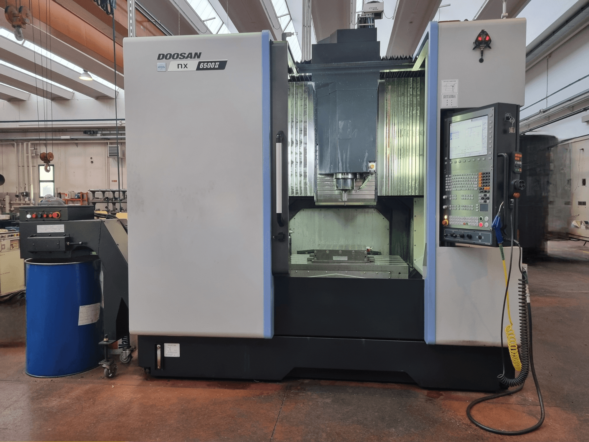 Верстат Doosan NX 6500 II з ЧПУ, вид спереду, з панеллю керування та зоною обробки, розташованою біля синьої бочки.