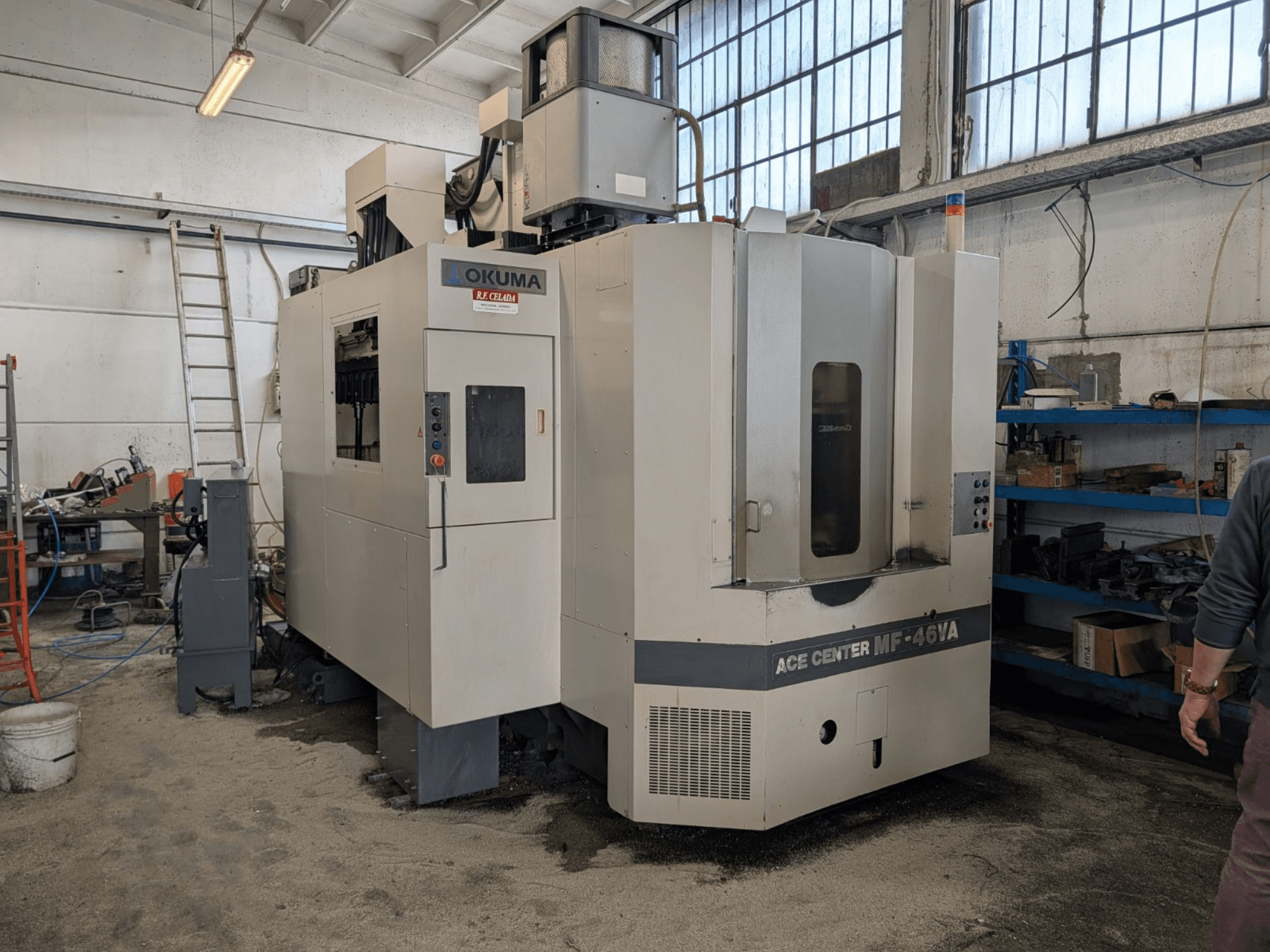 Вертикальний обробний центр Okuma ACE CENTER MF-46VA в майстерні, вид спереду з панеллю керування та навколишнім обладнанням.