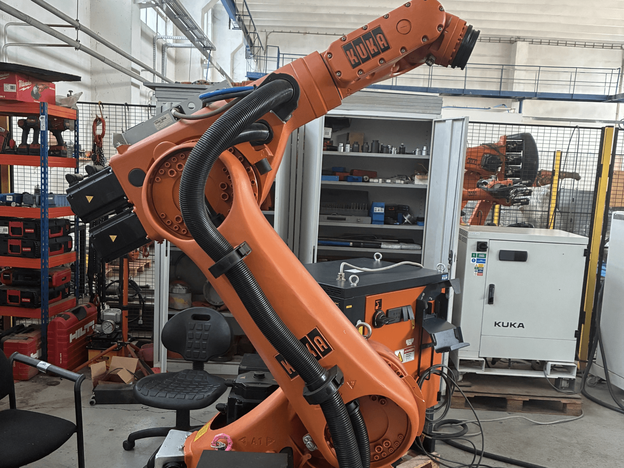 Робот-маніпулятор KUKA KR30-3 в промислових умовах, вид збоку з кабелями та елементами керування, на задньому плані - інструменти та стелажі.