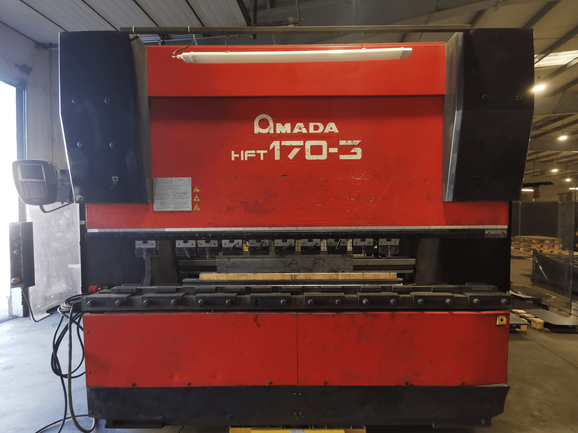 Червоний листозгинальний прес Amada HFT 170-3 вид спереду, показана панель управління, згинальні інструменти та робоча поверхня.