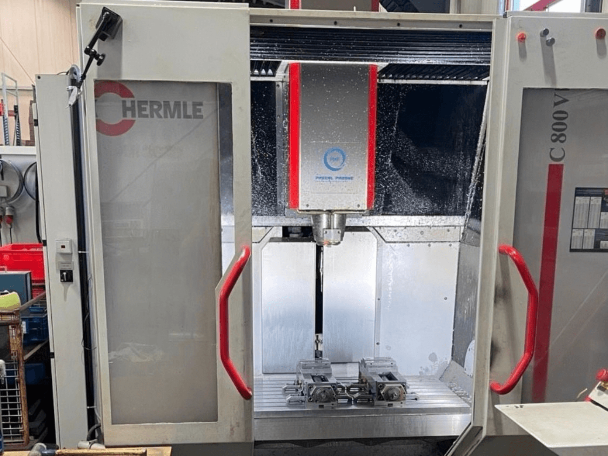 Вертикальний обробний центр HERMLE C800V, вид спереду, на якому видно зону обробки з заготовками та рідиною для охолодження.