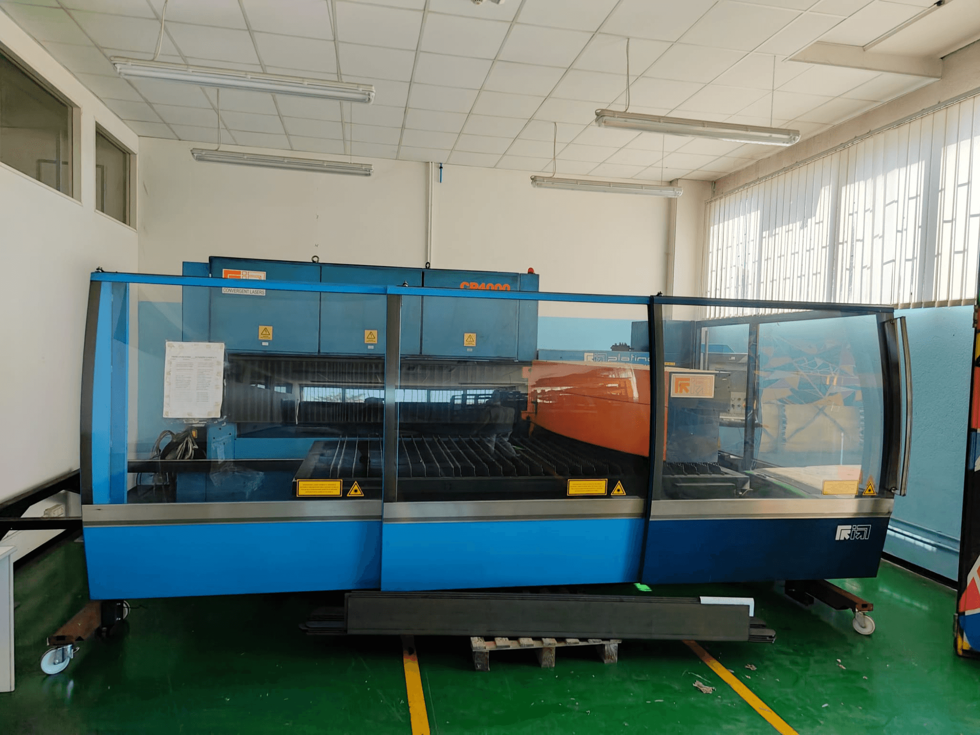 Вигляд спереду лазерного верстата для різання CONVERGENT LASERS CP4000 з CO2-лазером у синьо-помаранчевому кольорі в добре освітленому цеху.