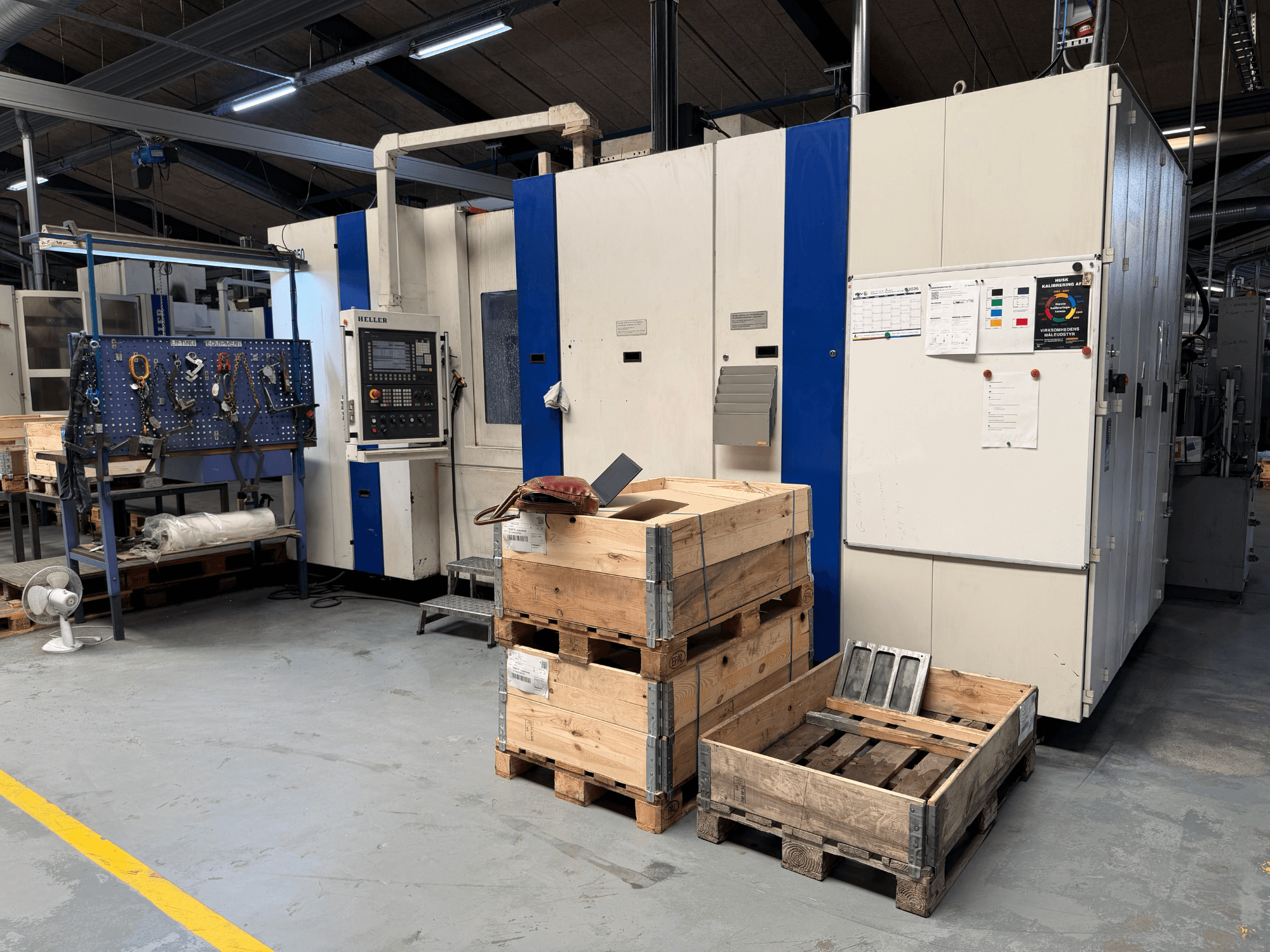 ГОРИЗОНТАЛЬНИЙ ОБРОБНИЙ ЦЕНТР HELLER MCH 250 в майстерні, вид збоку, видно дерев'яні піддони та стелаж для інструментів.