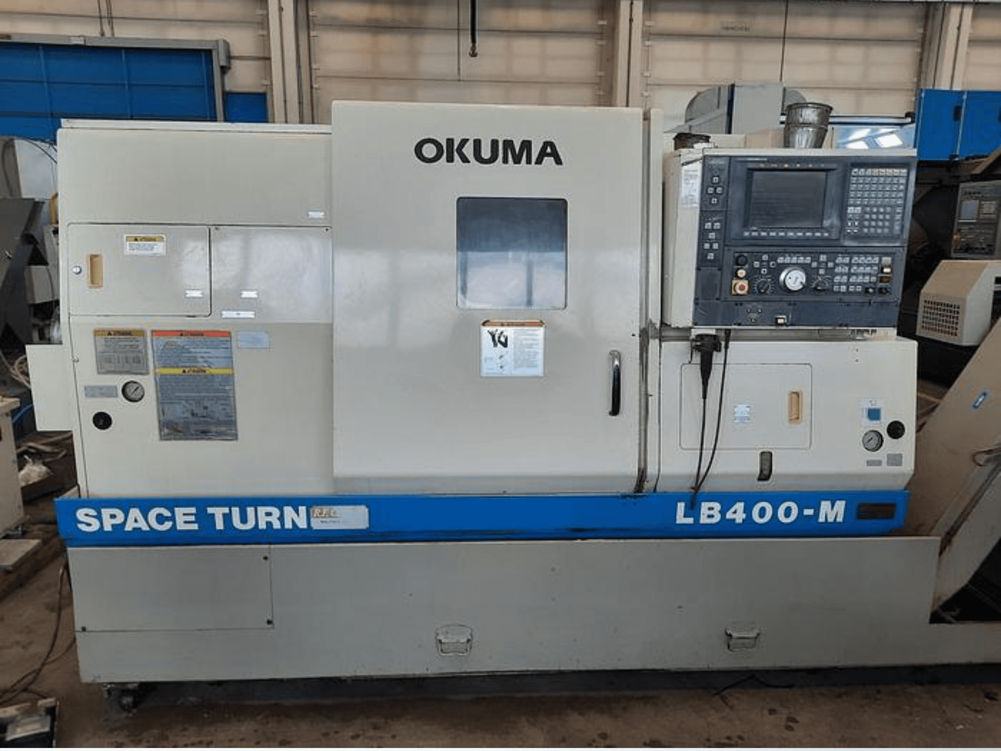 Токарний верстат з ЧПУ Okuma LB400-M, вид спереду з панеллю керування, попереджувальними етикетками та синім брендуванням "SPACE TURN".