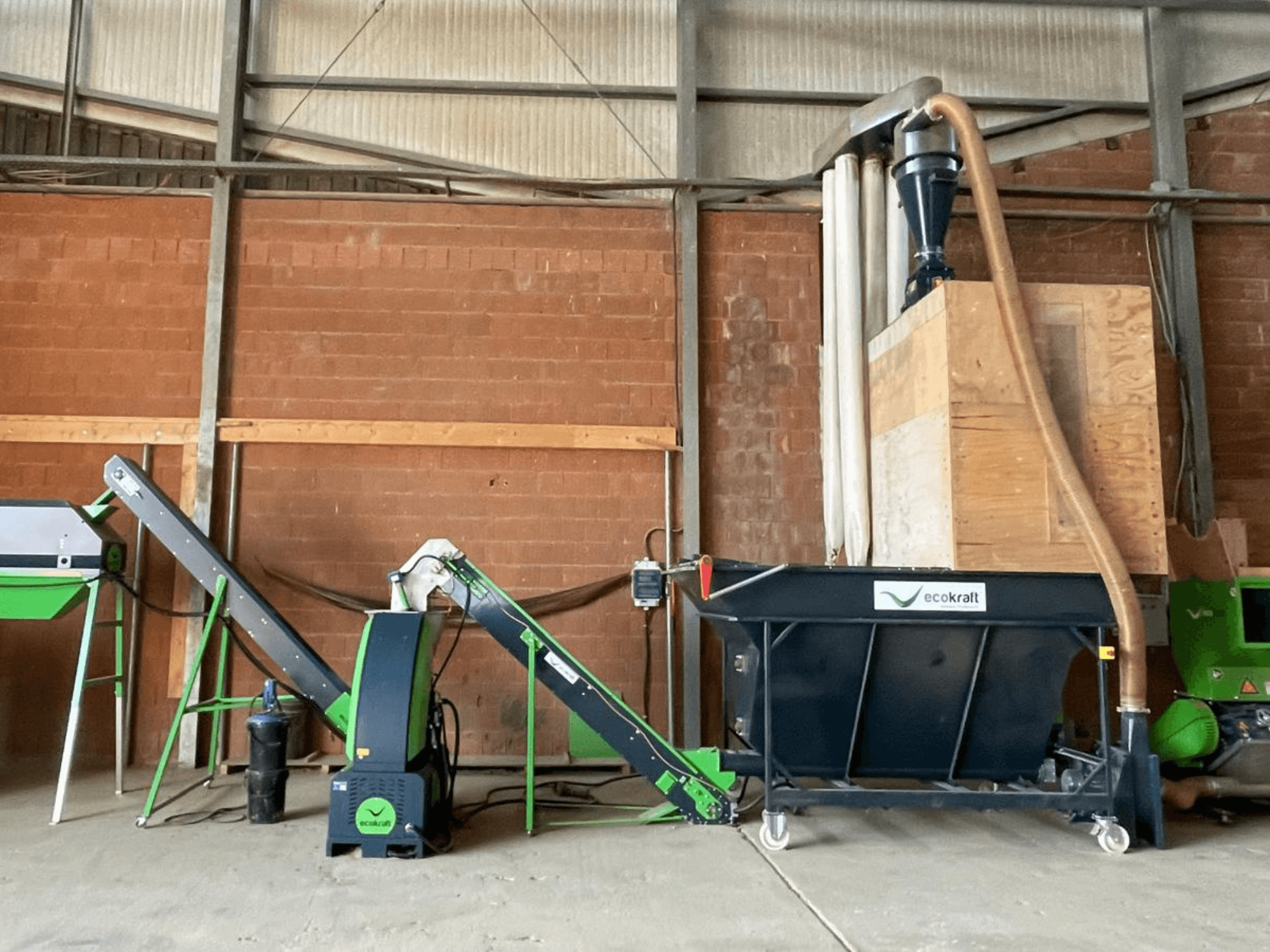 Верстат ECOKRAFT LP 22 на складі, оснащений конвеєром та системою пиловідведення. Вигляд збоку, на якому видно функціональні компоненти.