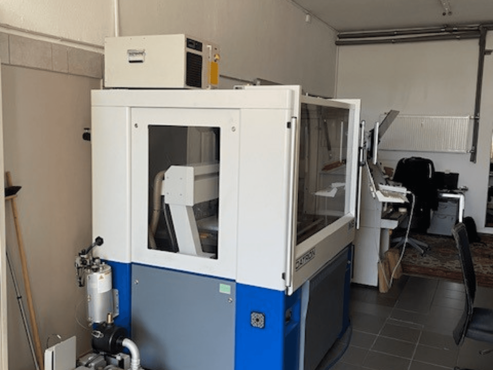 Синьо-біла промислова машина з прозорими панелями, вид спереду, включає доступ до управління і видимий вентиляційний блок.