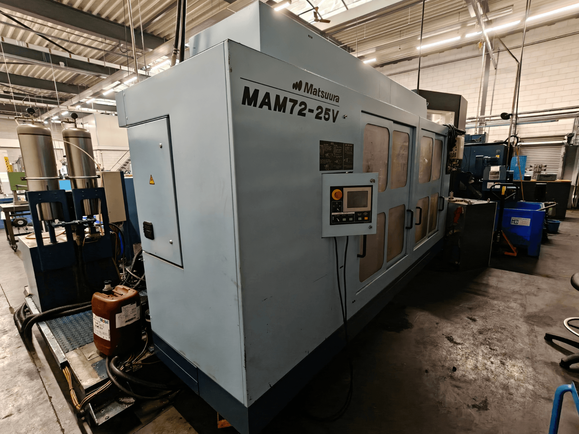 Верстат з ЧПК Matsuura MAM72-25V, вид збоку, оснащений панеллю керування, двома баками для охолоджувальної рідини та робочим простором у промислових умовах.