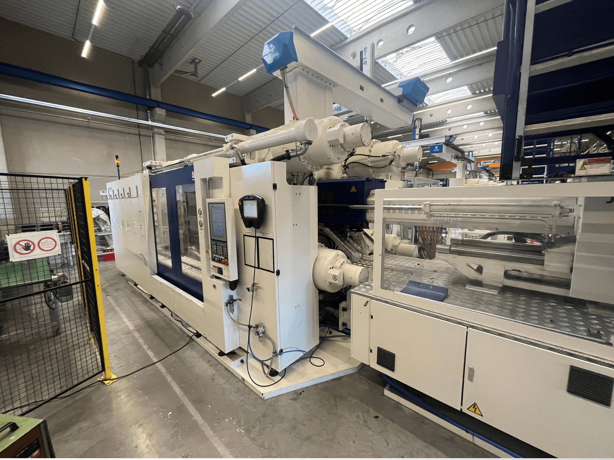 Термопластавтомат біло-синього кольору, вид спереду, з панеллю керування, роботизованою рукою та знаками безпеки.