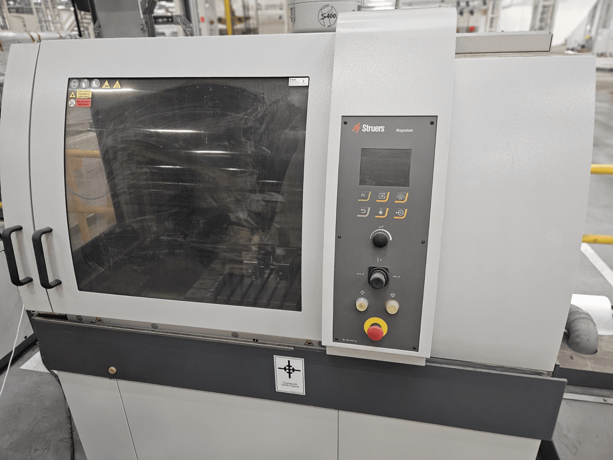 Вид спереду машини Struers Magpentor з панеллю керування, кнопками та великим оглядовим вікном. Видно технічні етикетки.