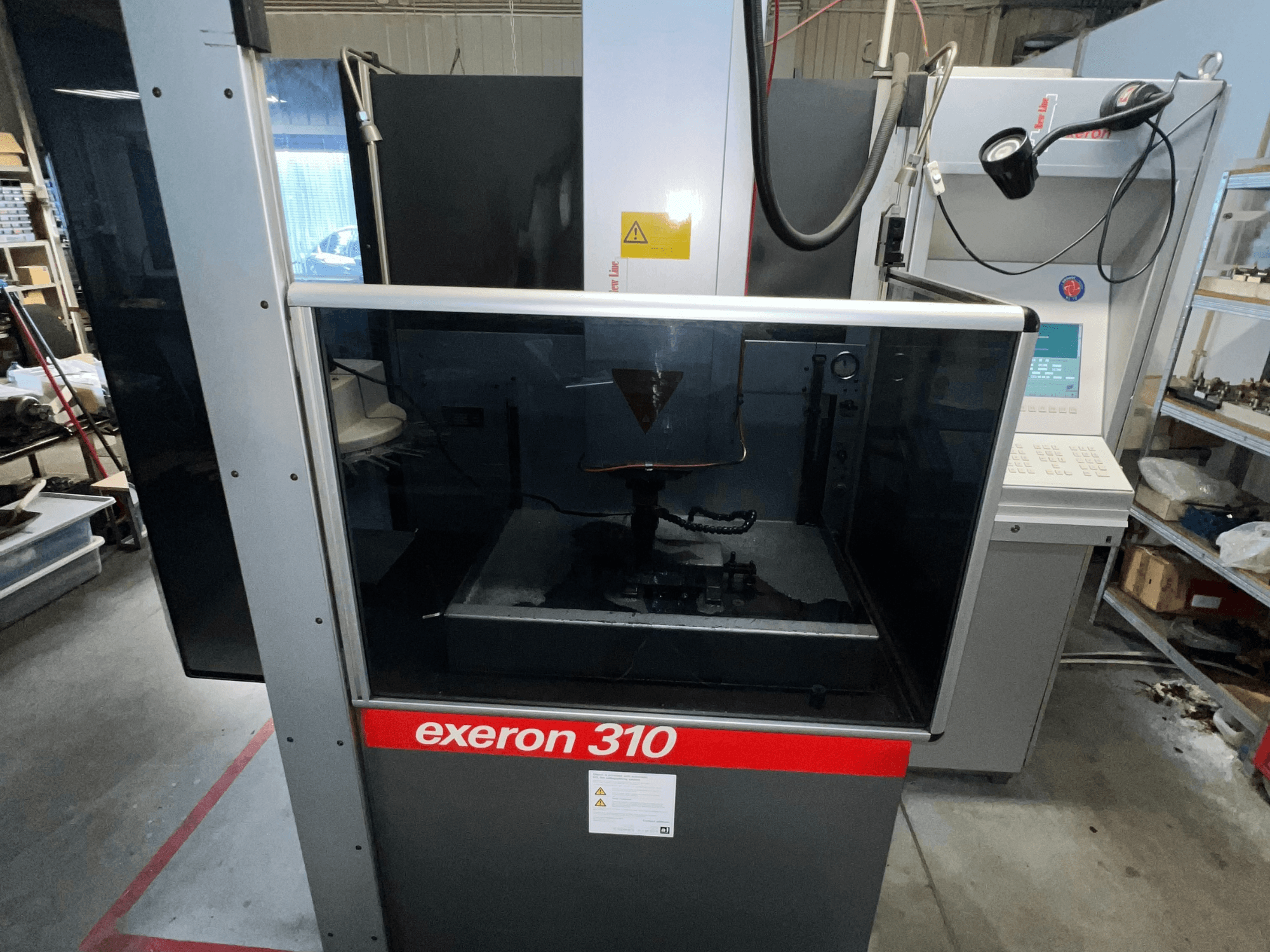 Вид спереду на машину Exeron 310, що демонструє скляну камеру і панель управління поряд зі стелажами робочої станції.
