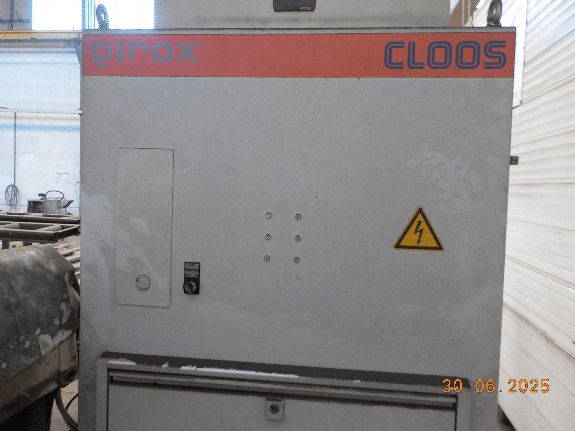 Зварювальний апарат Cloos QIROX збоку, з панеллю керування та попереджувальним знаком, з запиленою поверхнею та видимим штампом дати.