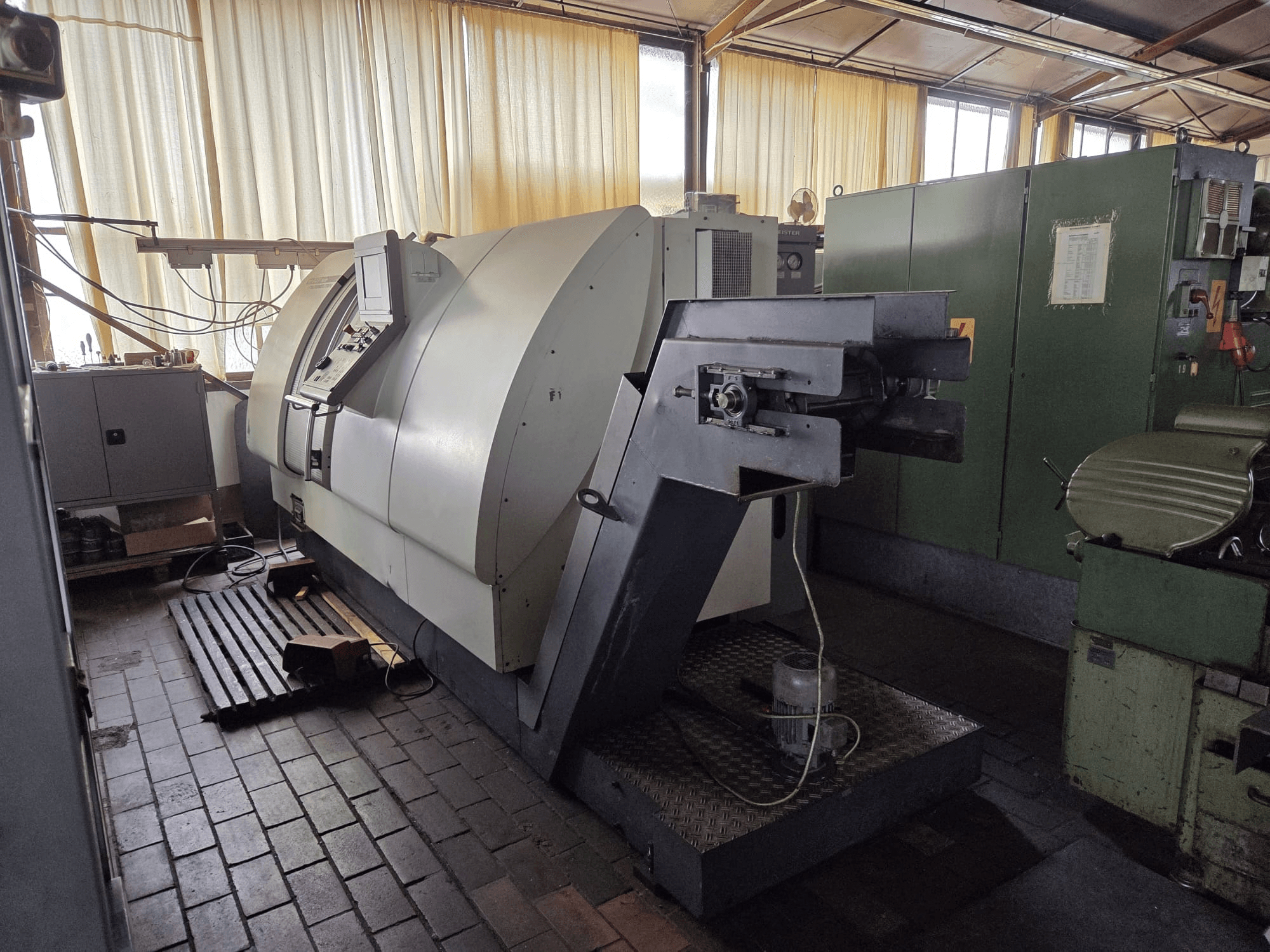 Двофункціональний токарно-фрезерний центр Gildemeister CTX 400, вид збоку, на якому видно панель управління, велике шасі та сусіднє обладнання в цеху.