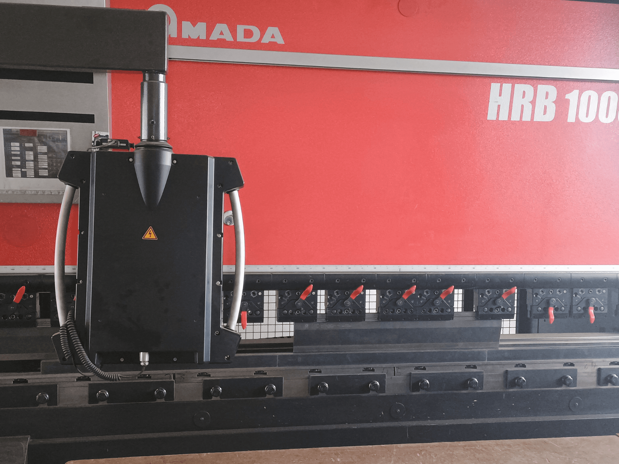 Згинальний верстат Amada HRB 100 вид спереду; оснащений чорною головкою управління з конічним соплом і регульованими затискачами.