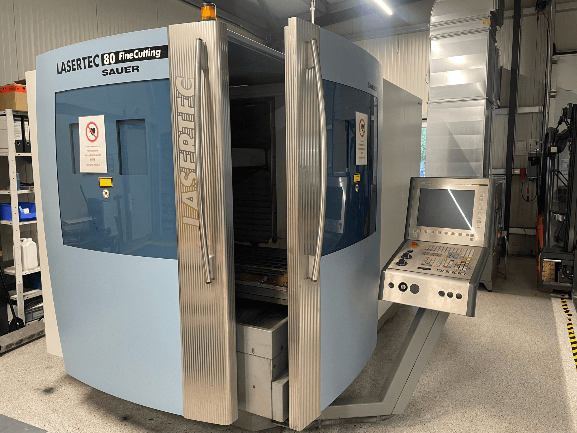 Вигляд спереду верстата для точного різання листового металу DMG Sauer Lasertec80 FineCutting з панеллю керування, відкритими дверцятами та помітними знаками безпеки.