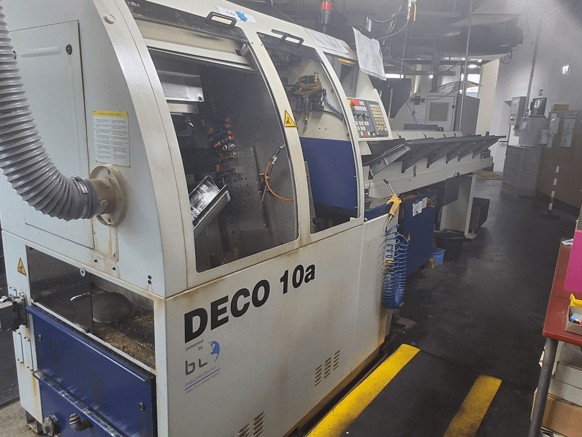 Токарний верстат швейцарського типу TORNOS DECO 10a, вид спереду; має панель управління, видимі механізми і трубку для відсмоктування пилу.
