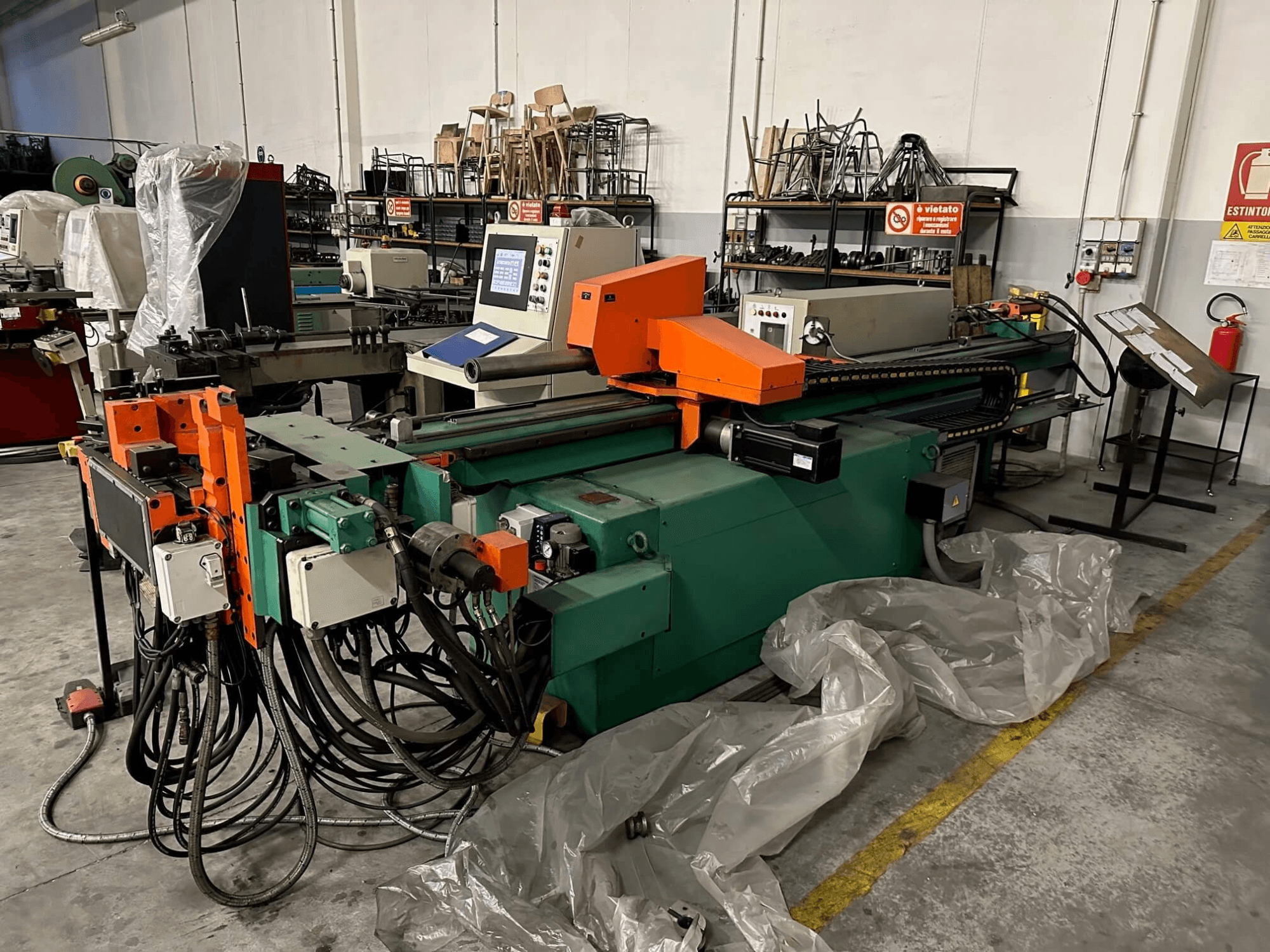 Промислова машина з помаранчево-зеленим корпусом, панеллю керування та численними кабелями, вигляд спереду в умовах майстерні.