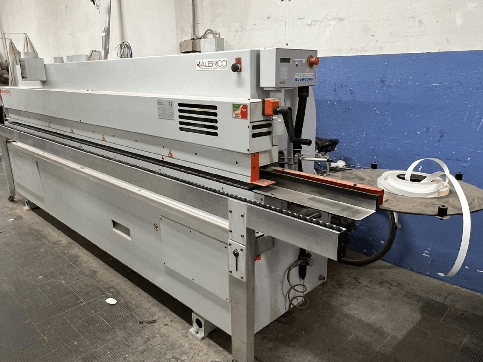 Кромкооблицювальна машина ALBRICO з видом спереду, з довгою конвеєрною стрічкою і прикріпленим рулоном клейкої стрічки.