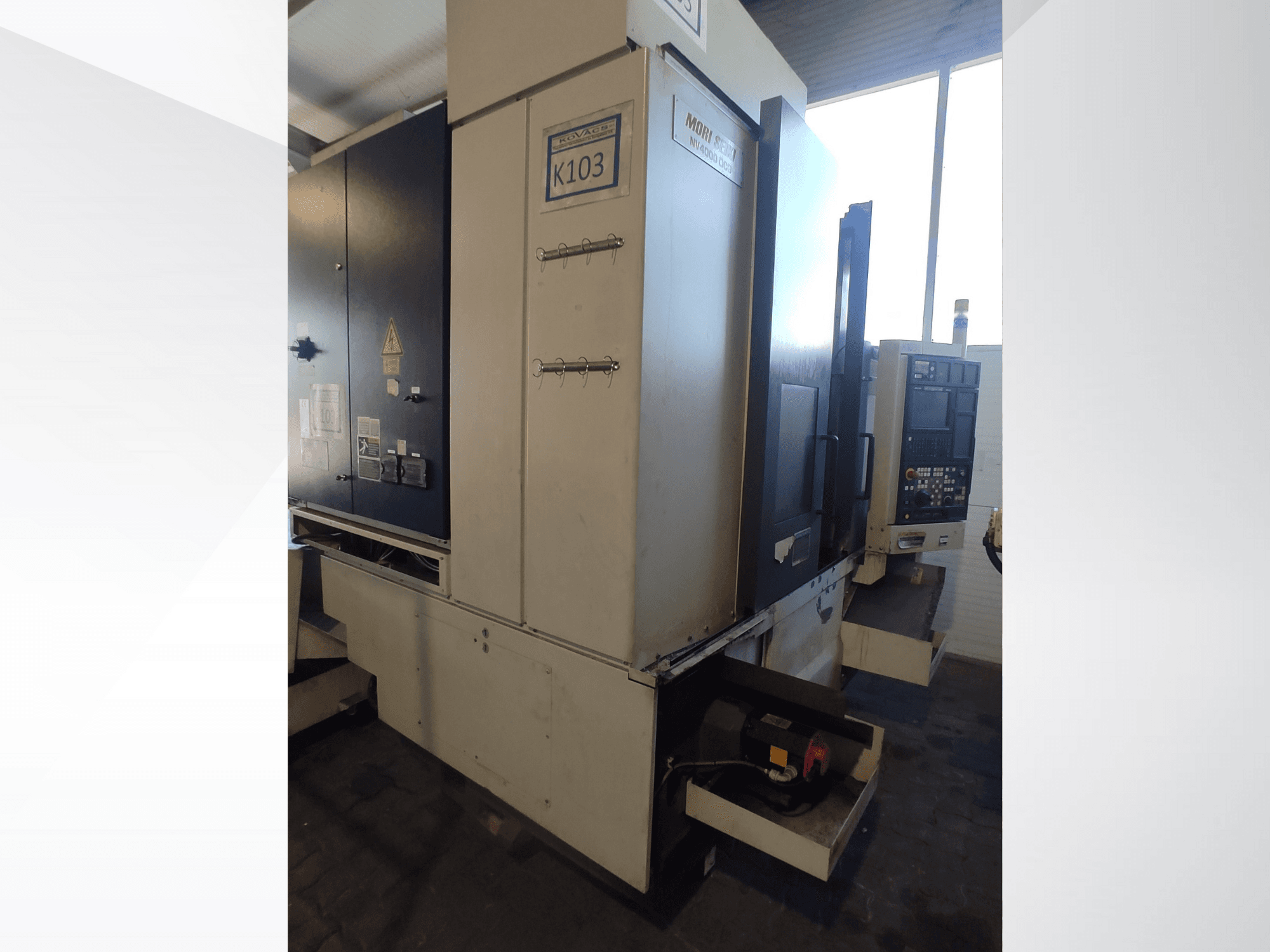 Верстат з ЧПК Mori Seiki K103 спереду, з панеллю керування, етикетками безпеки та електричними компонентами.