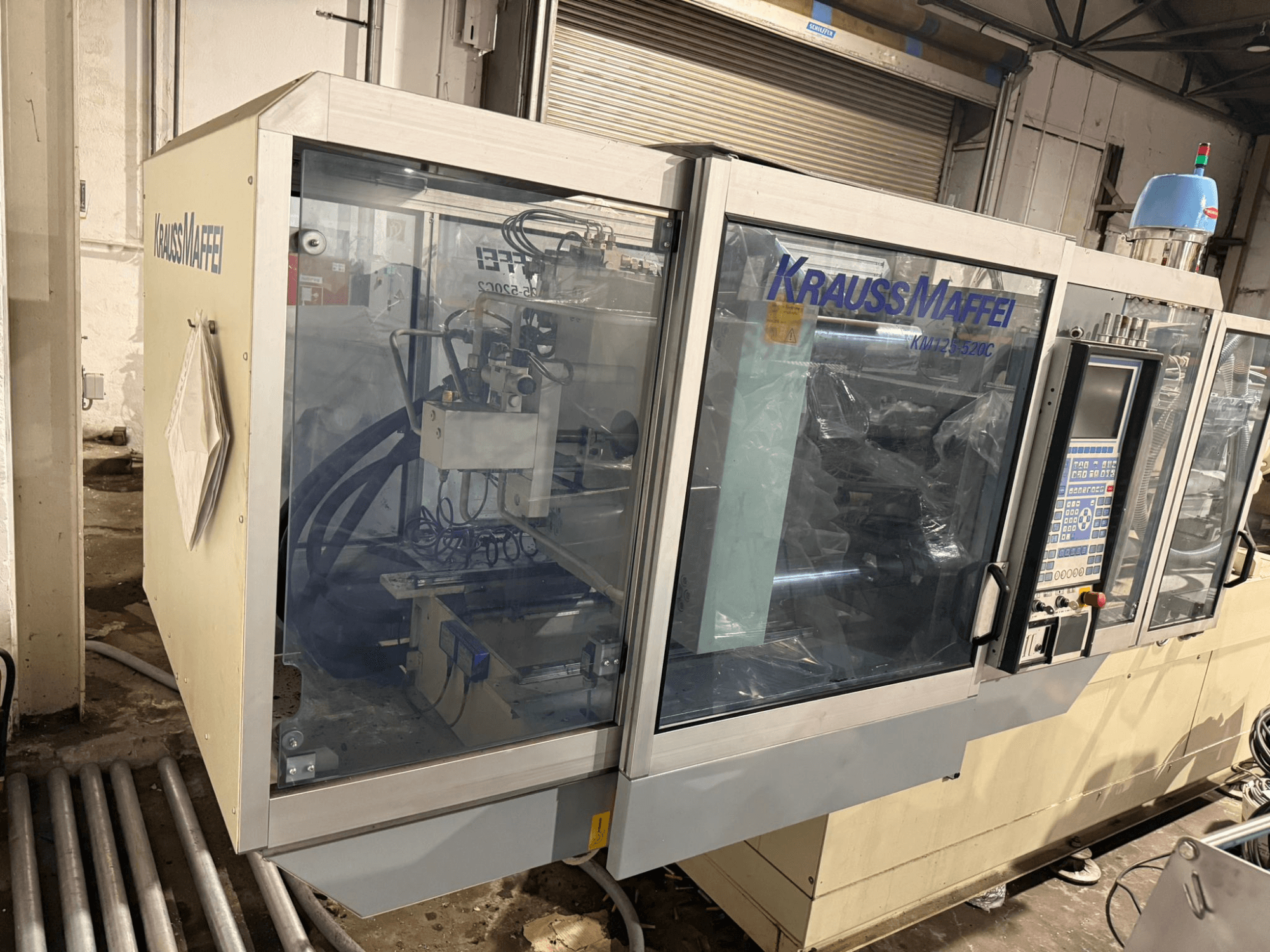Гідравлічний термопластавтомат Krauss Maffei KM125-520C2, вигляд спереду з панеллю керування та прозорим корпусом.