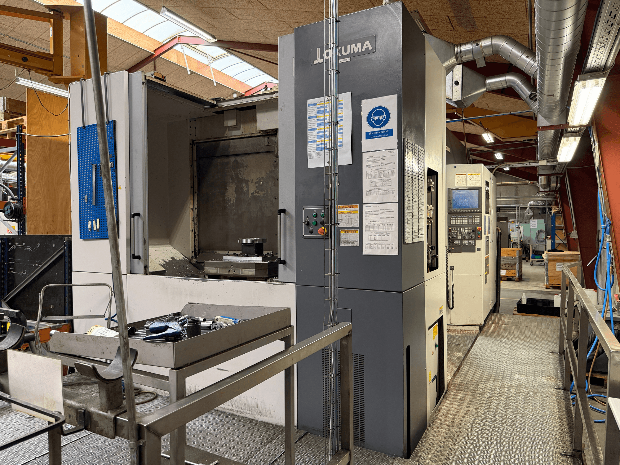 Горизонтальний обробний центр Okuma MA-600HB, вид спереду, на якому видно інструменти на металевому столі та органи управління верстатом.
