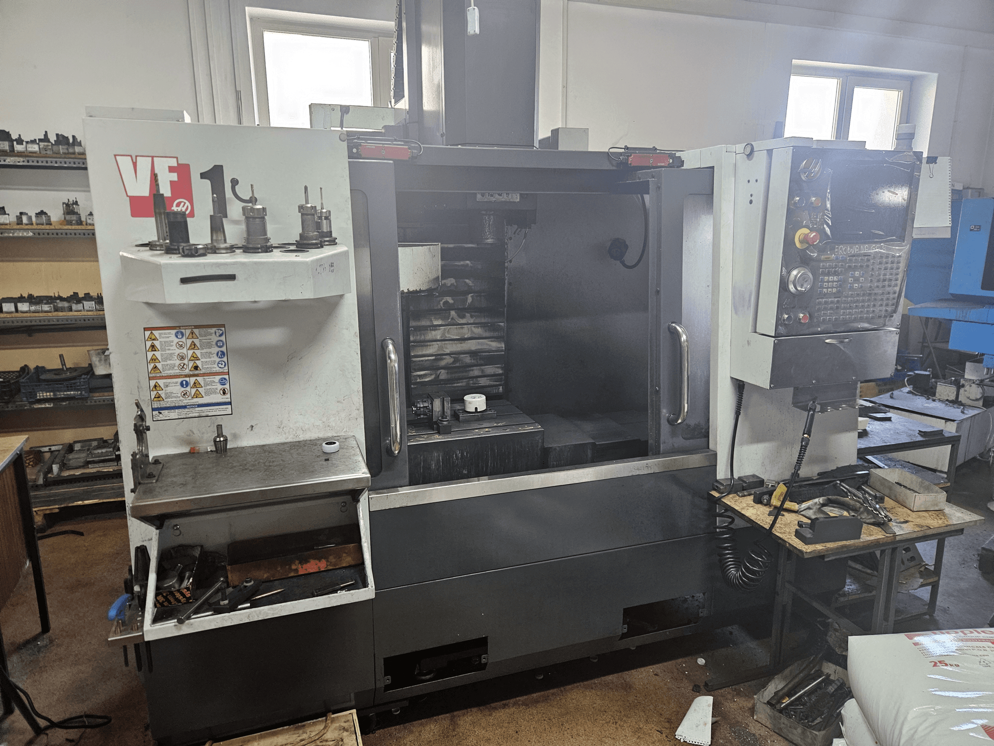 Вертикальний обробний центр HAAS VF-1, вид спереду з інструментами збоку, видно панель керування та робочий простір на задньому плані.