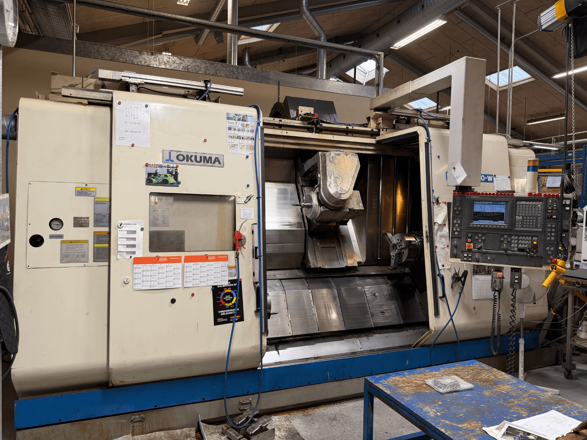 Токарно-фрезерний центр Okuma MacTurn350-W, вид спереду, на якому видно панель управління та відкритий доступ до зони обробки.
