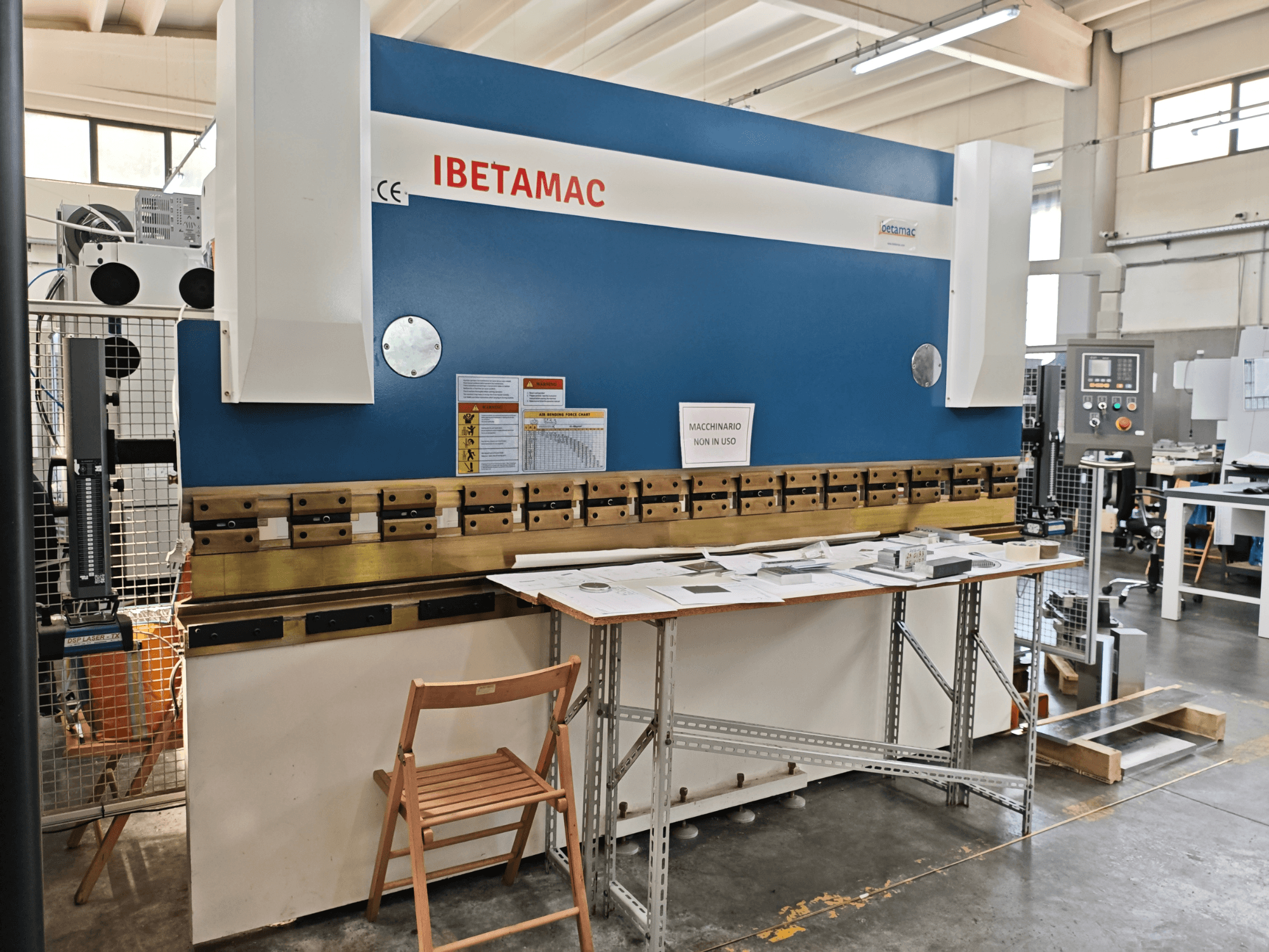 Прес-згинальний верстат IBETAMAC 3200 100T у цеху, вид збоку, на якому видно панель управління, робочу зону та попереджувальні написи.