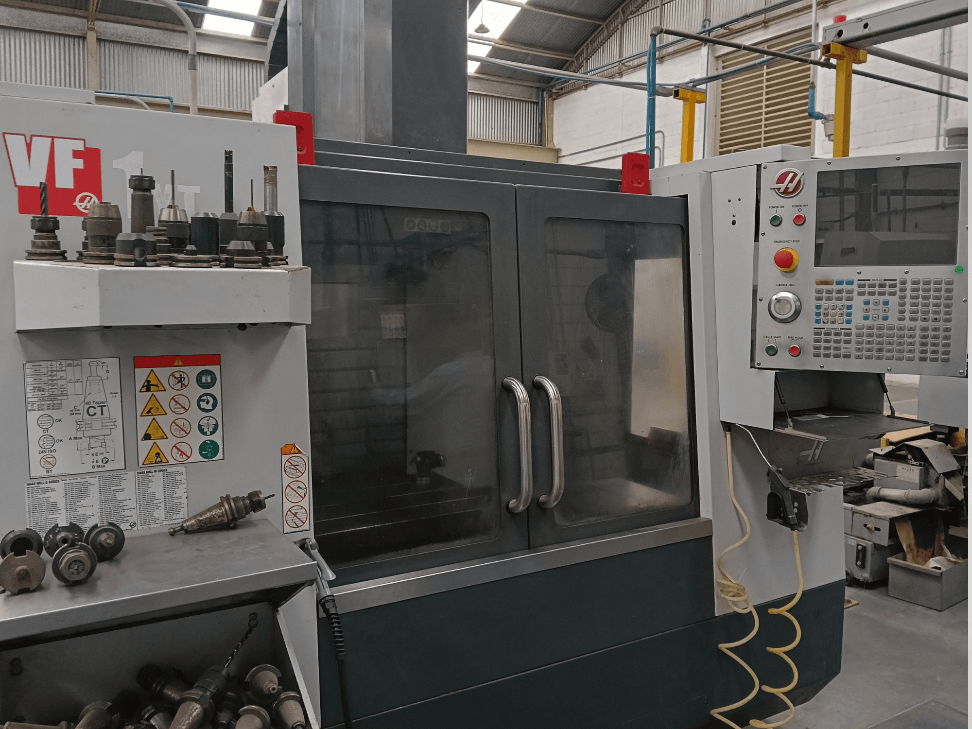 Вертикальний обробний центр HAAS VF-1YT-3 у фронтальному ракурсі, на якому видно органи управління, тримачі інструментів та захисні наклейки.