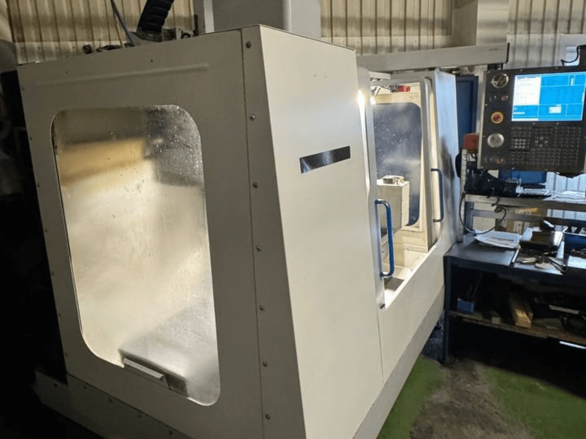 Вертикальний обробний центр HAAS VCE 750 у вигляді збоку, з панеллю керування та прозорим захисним кожухом.