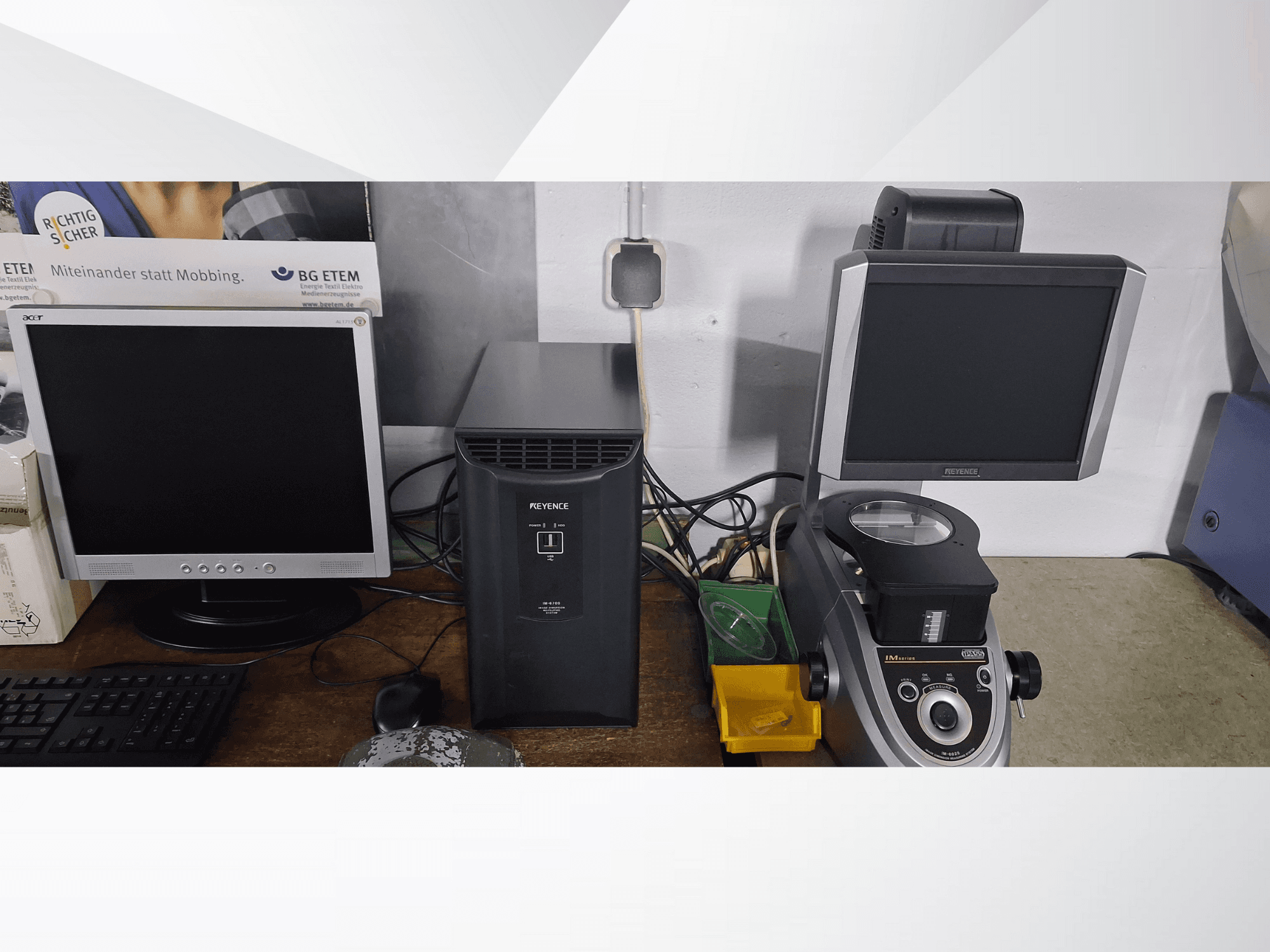 Два комп'ютерні монітори, один Acer і один Keyence, поруч з чорним пристроєм і мікроскопом, вид спереду.