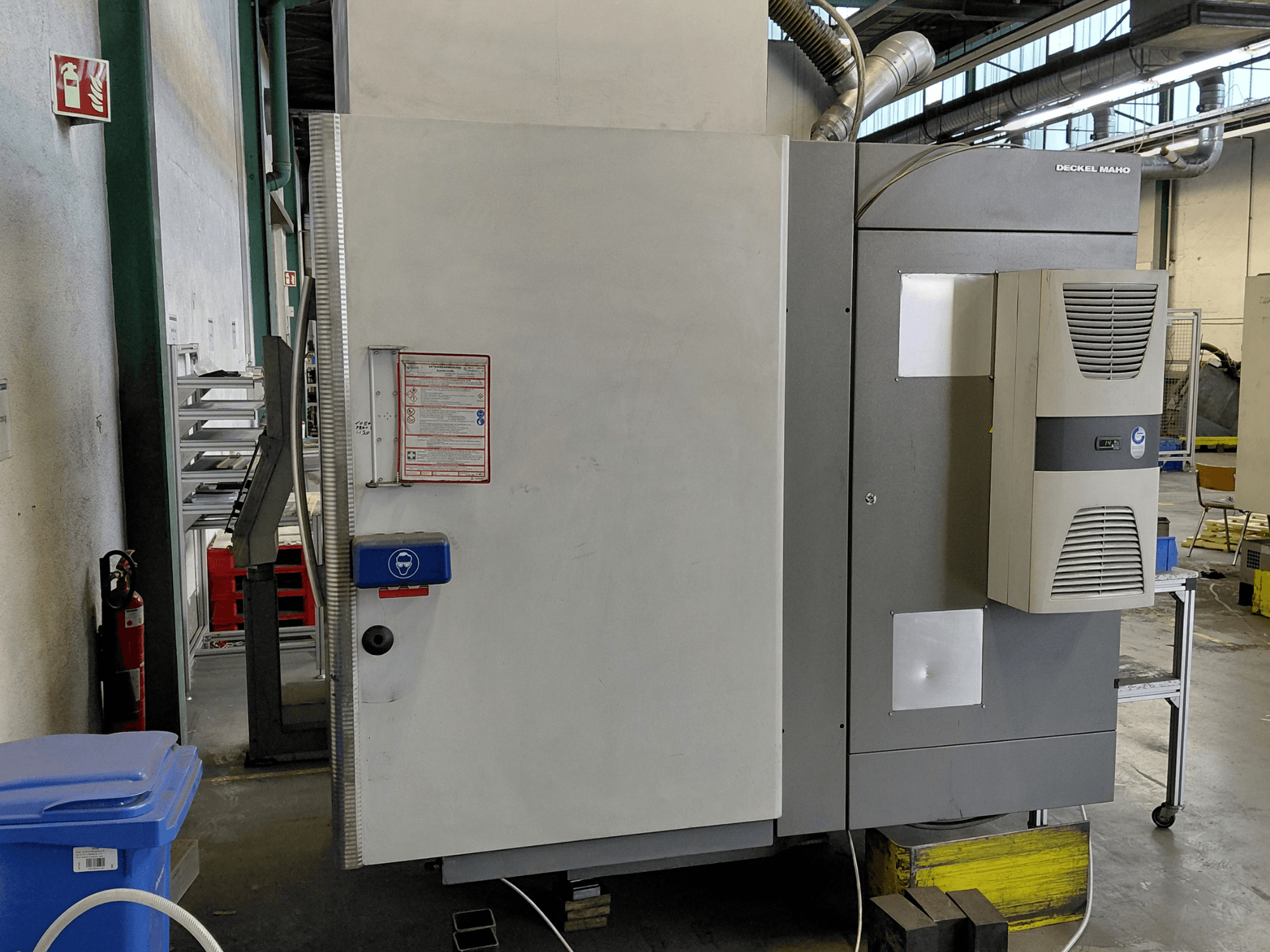 Вид збоку вертикального обробного центру DECKEL MAHO DMC 635 V з панеллю керування та етикетками безпеки.