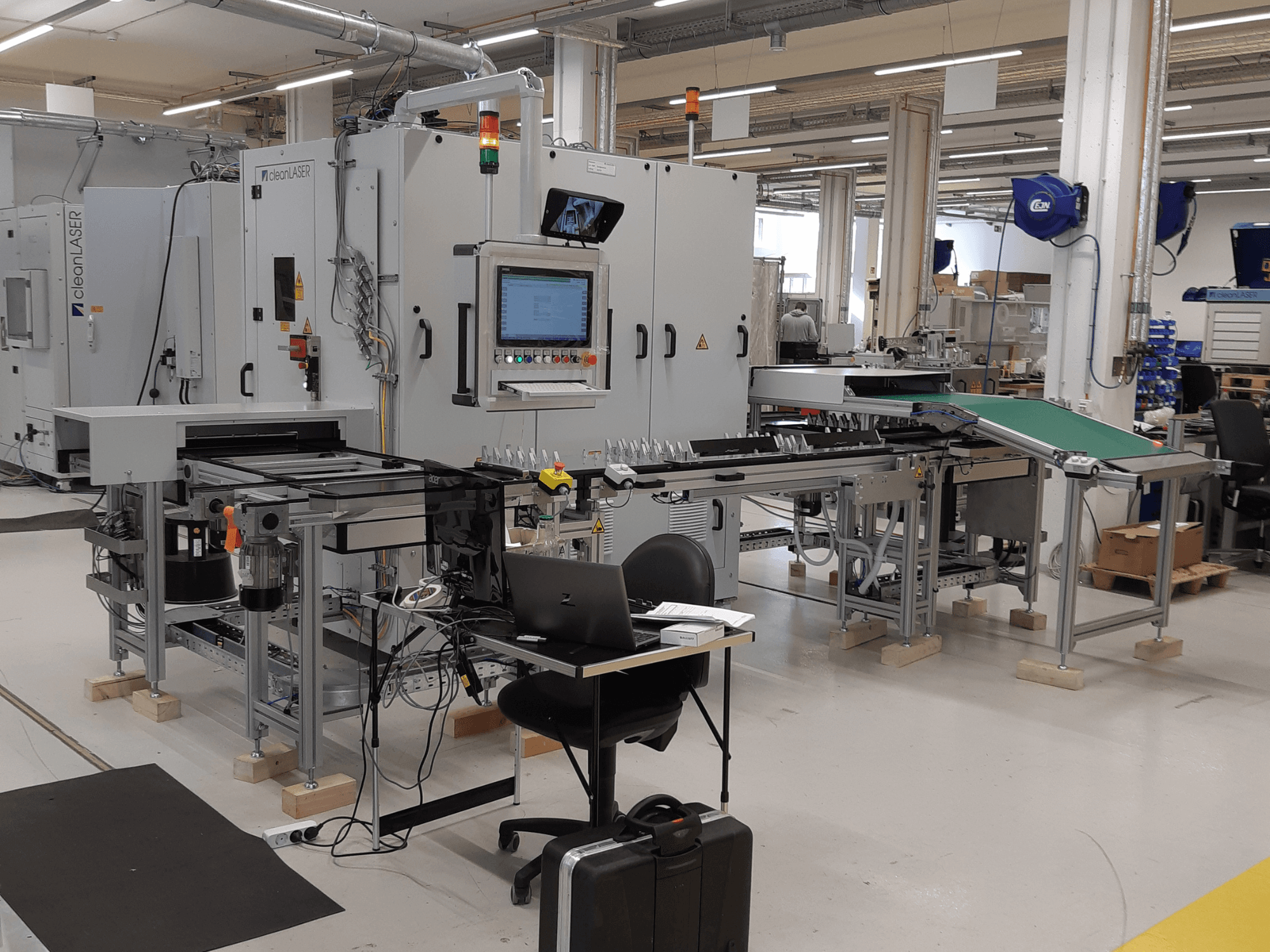 Верстат CLEAN LASER clean CELL 3220 CL600, вид спереду, з панеллю керування, конвеєром та робочою зоною, у цехових умовах.