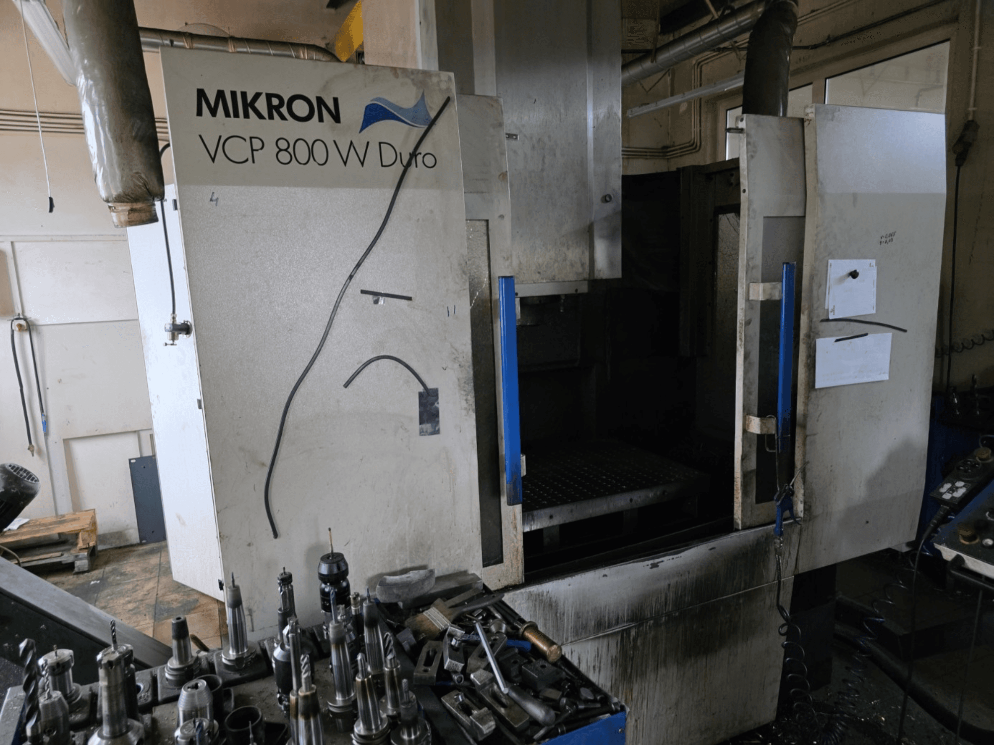 Фрезерний верстат Mikron VCP 800 Вт Duro показаний збоку, на передньому плані видно інструменти та елементи керування.