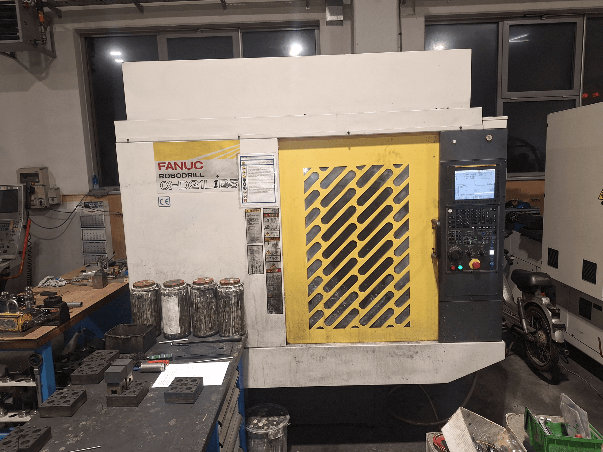 Вид спереду FANUC Robodrill α-D21LiB5: панель керування, жовта решітка та інструменти на робочому столі.