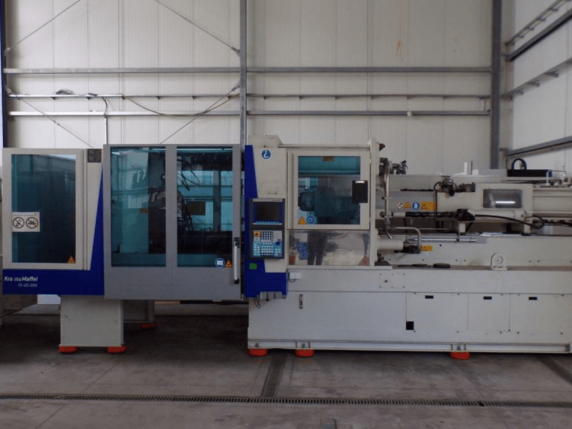 Термопластавтомат KraussMaffei, вид збоку, з панеллю керування та індикаторами безпеки, видимими на заводі-виробнику.