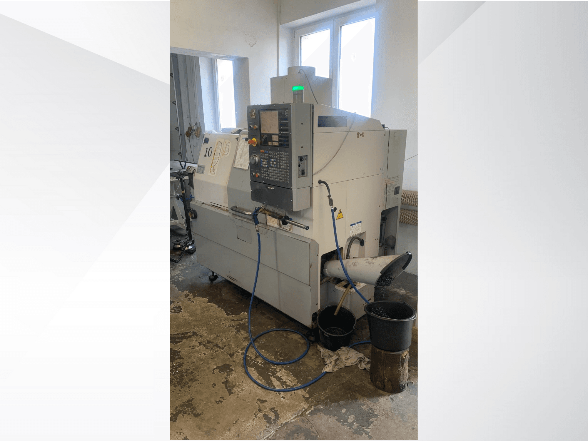 Модель верстата з ЧПК Haas з панеллю керування, вид збоку, з лінією подачі охолоджувальної рідини, жолобом для відходів і контейнерами для зберігання внизу.