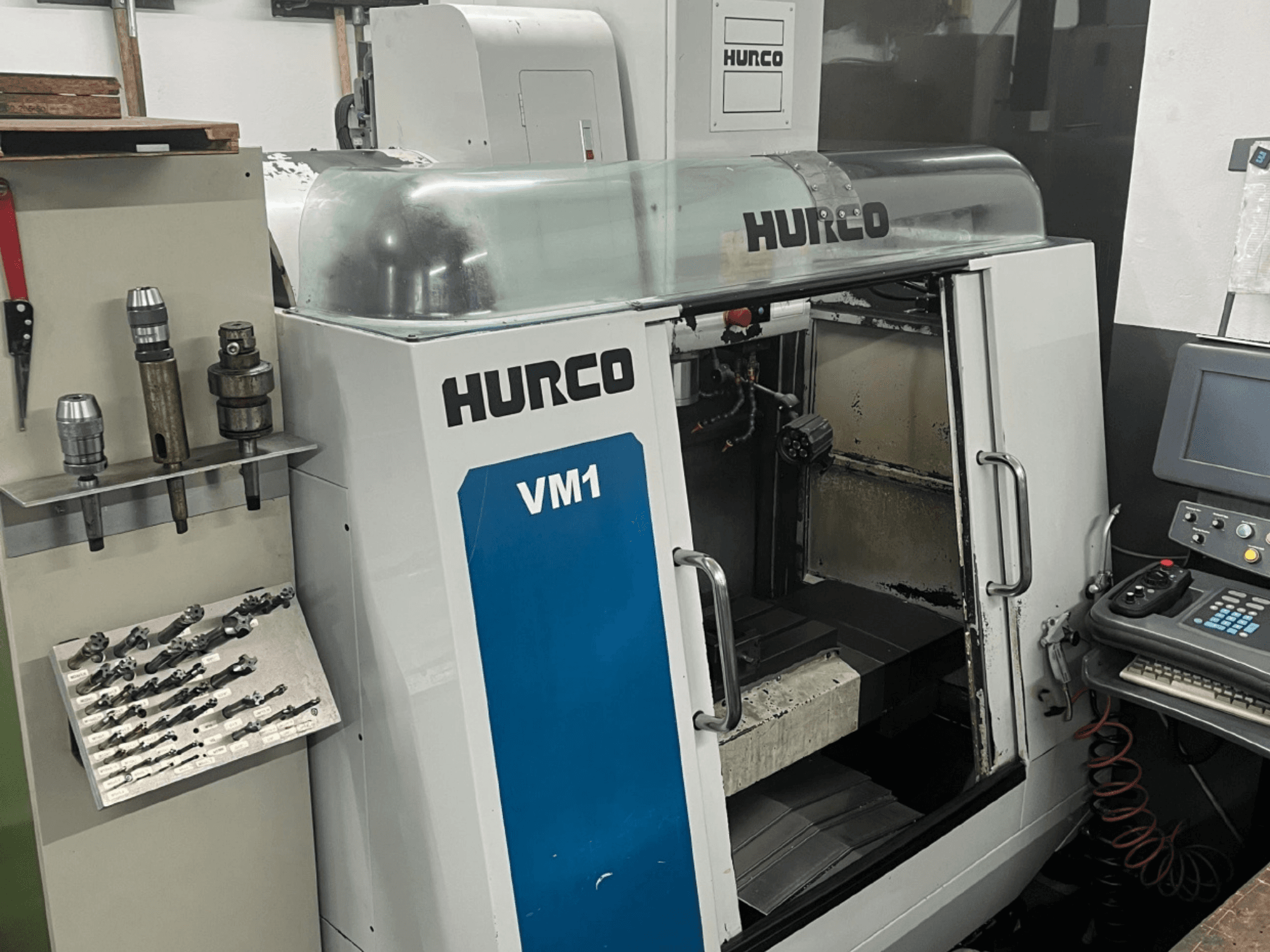 Вертикальний обробний центр Hurco VM1 спереду, з прозорою кришкою, панеллю керування та встановленими інструментами.