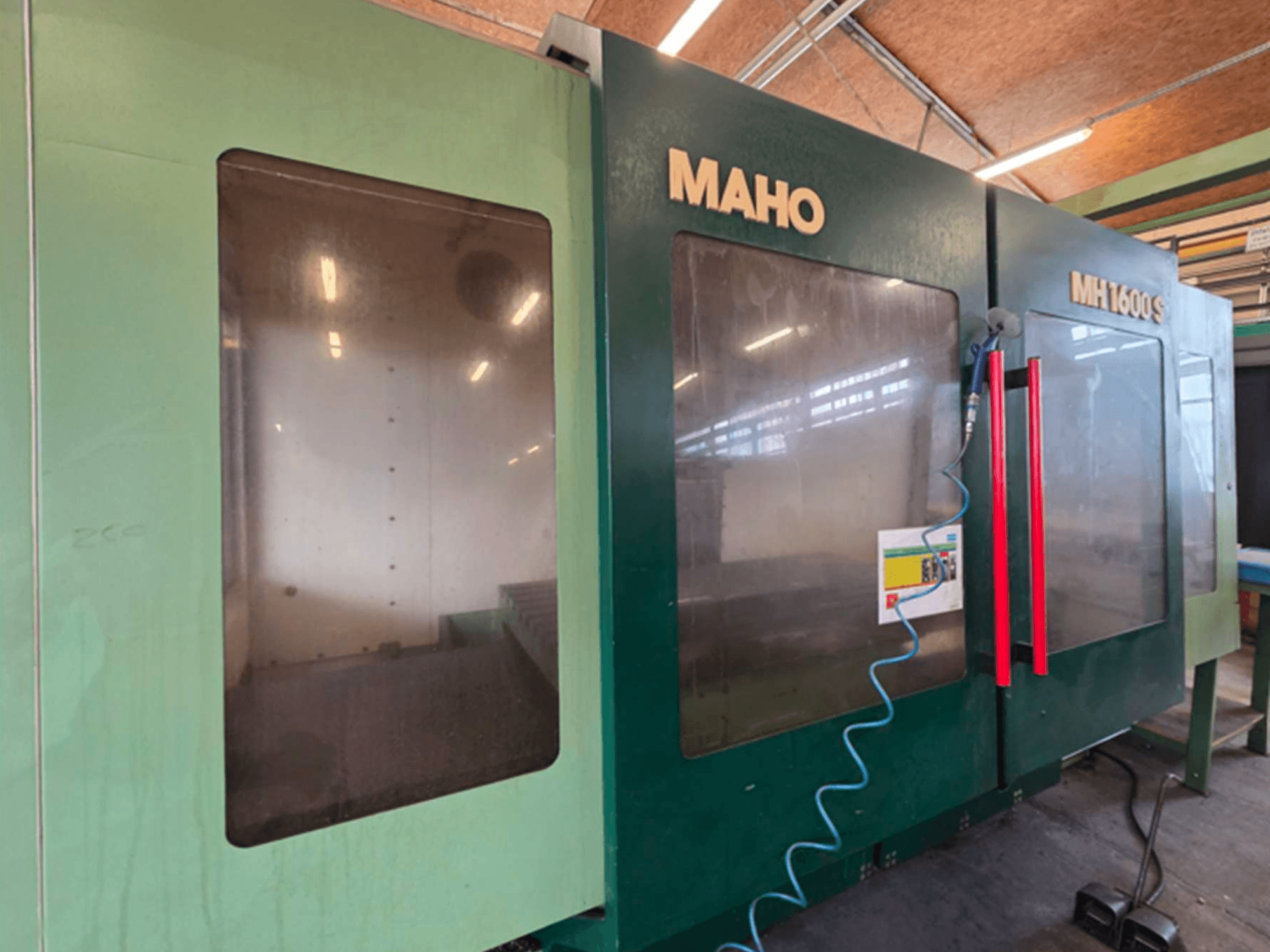 Універсальний обробний центр MAHO 1600S спереду, з двома прозорими панелями та панеллю керування з червоними ручками.