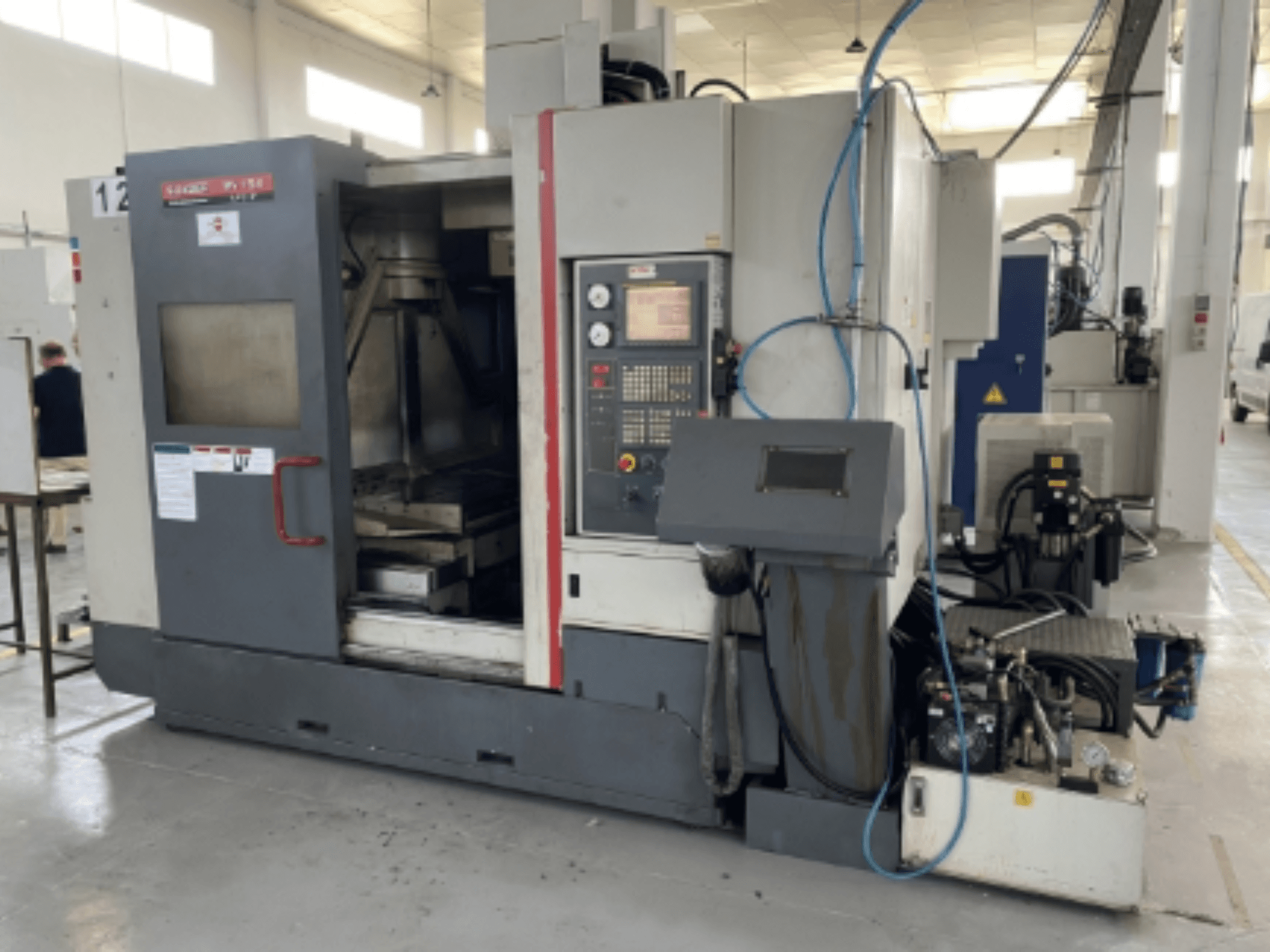 Вертикальний обробний центр Quaser MV154APC-912, вид спереду з панеллю керування, відкритими дверцятами та компонентами верстата.