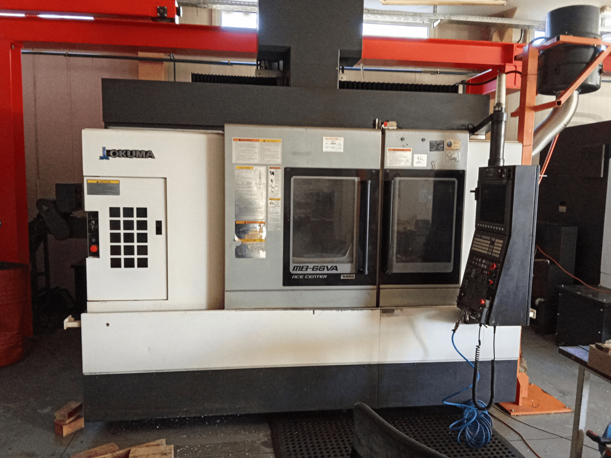 Вертикальний обробний центр Okuma MB-66VA, вид спереду з панеллю керування та двома оглядовими вікнами для доступу до інструменту.