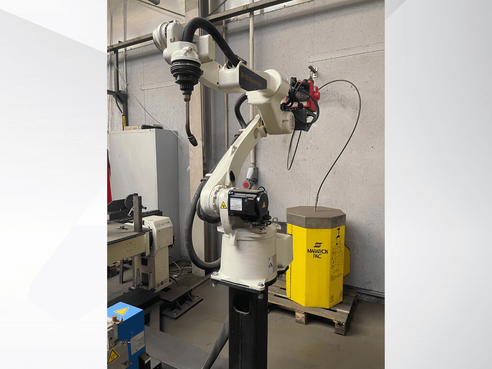 Роботизована рука Kawasaki збоку, з встановленим тримачем інструменту, з жовтим силовим блоком на задньому плані.