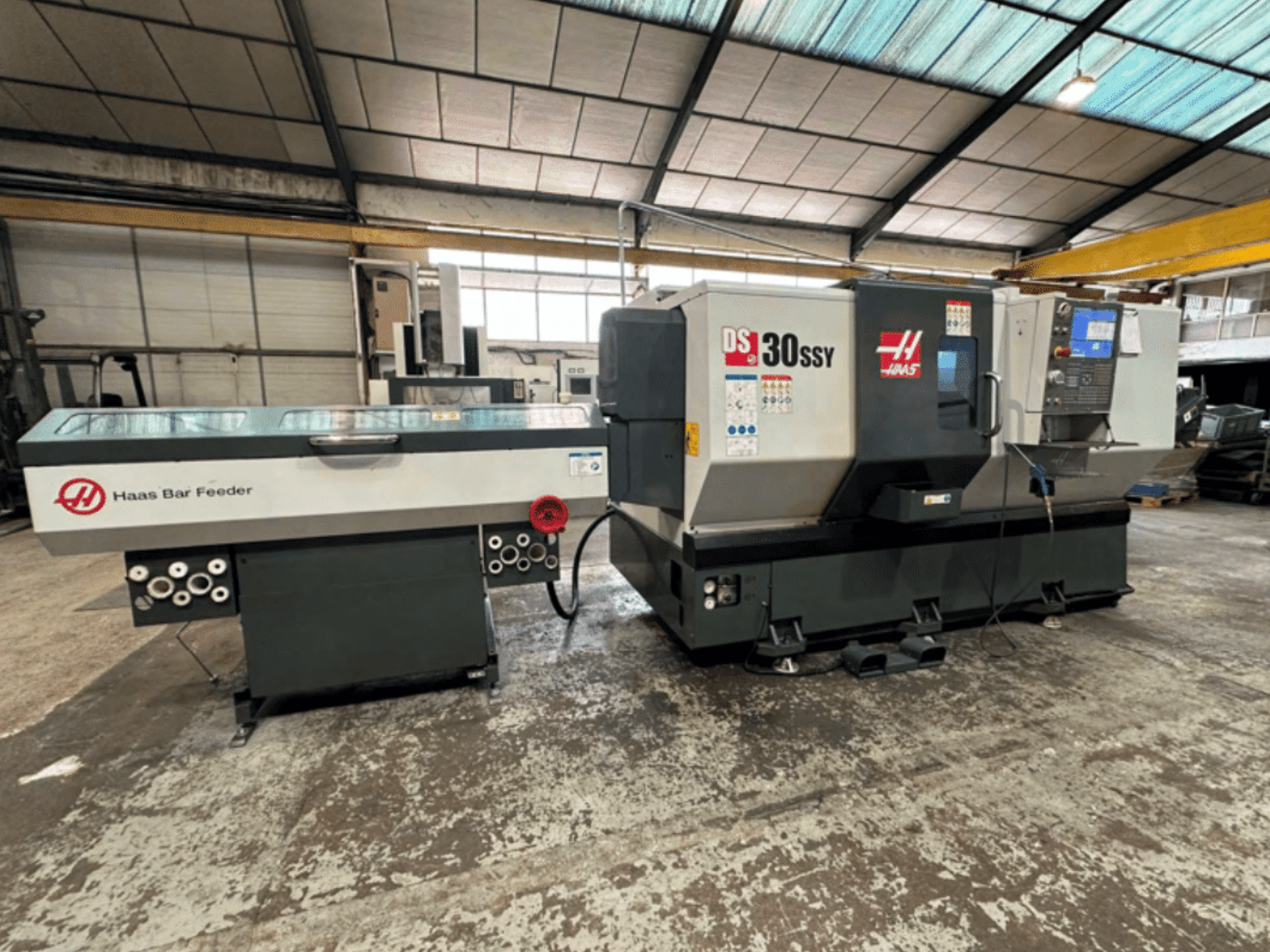 Токарний верстат з ЧПК Haas DS-30SSY з механізмом подачі прутка Haas, вид збоку, що демонструє панель керування та механізм подачі в умовах майстерні.