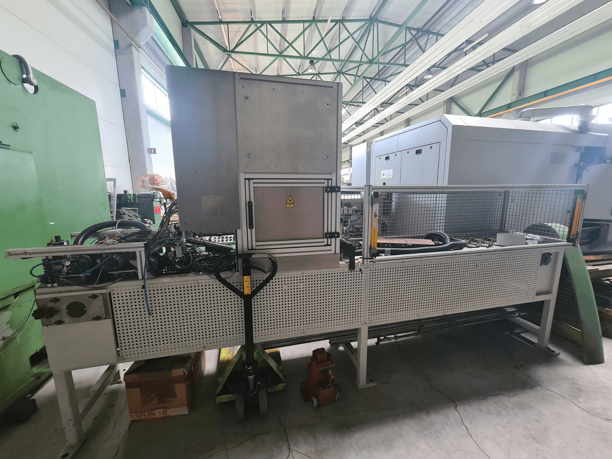 Промислове обладнання з металевою рамою, шлангами та панеллю керування, вигляд збоку в заводських умовах.