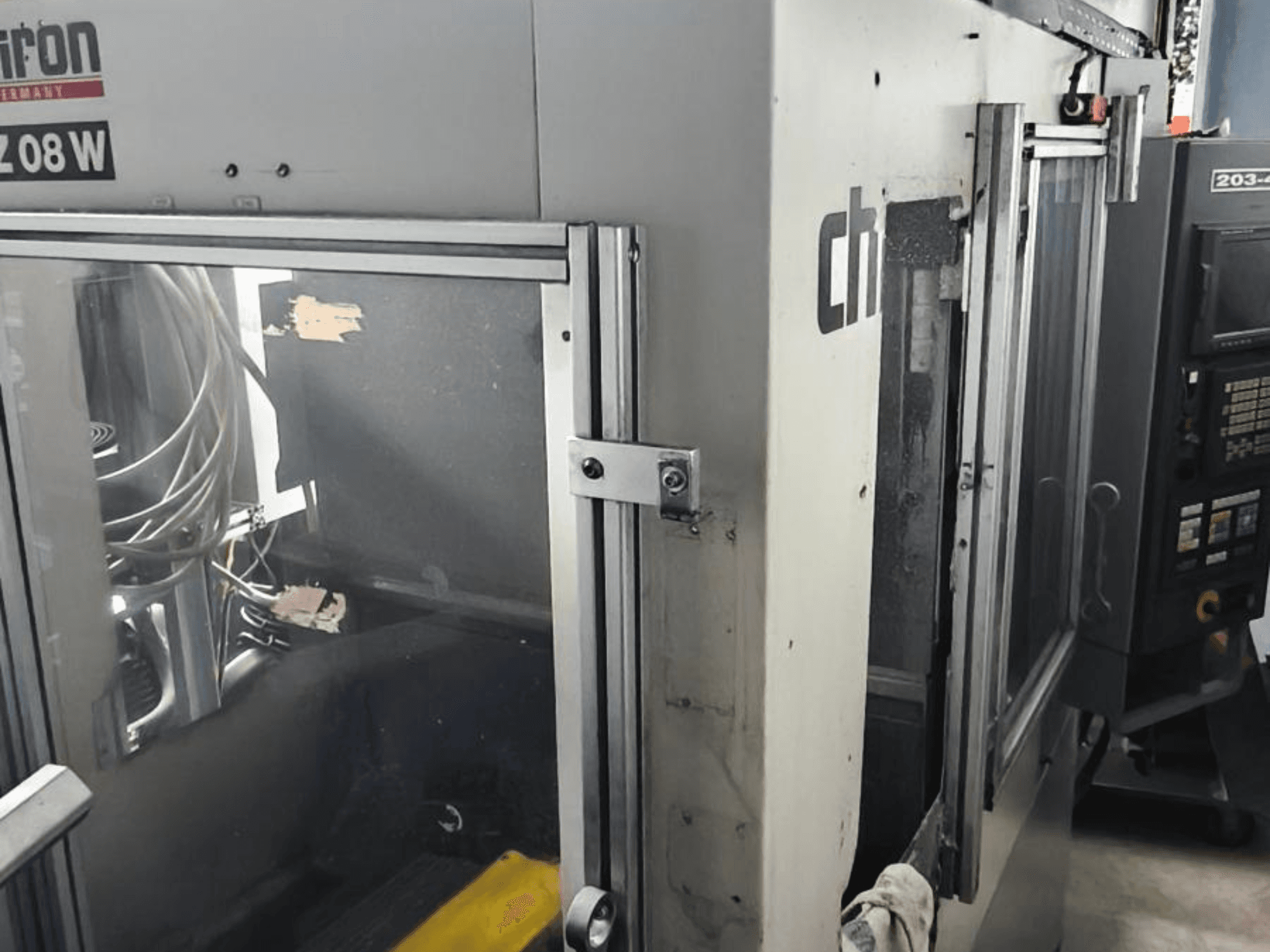 Вертикальний обробний центр CHIRON FZ 08 W, вид спереду з панеллю керування і частково відкритими дверима, з видимими внутрішніми компонентами.