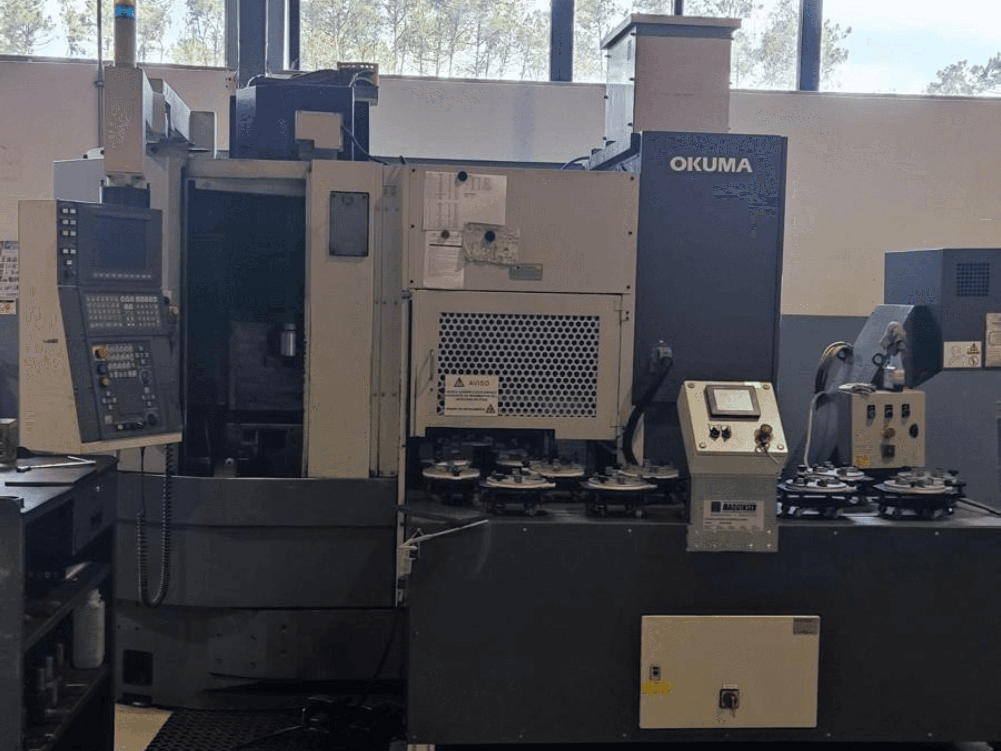 Вертикальний токарний верстат Okuma LVT300 спереду, з панеллю керування, тримачами інструменту та зоною обробки.