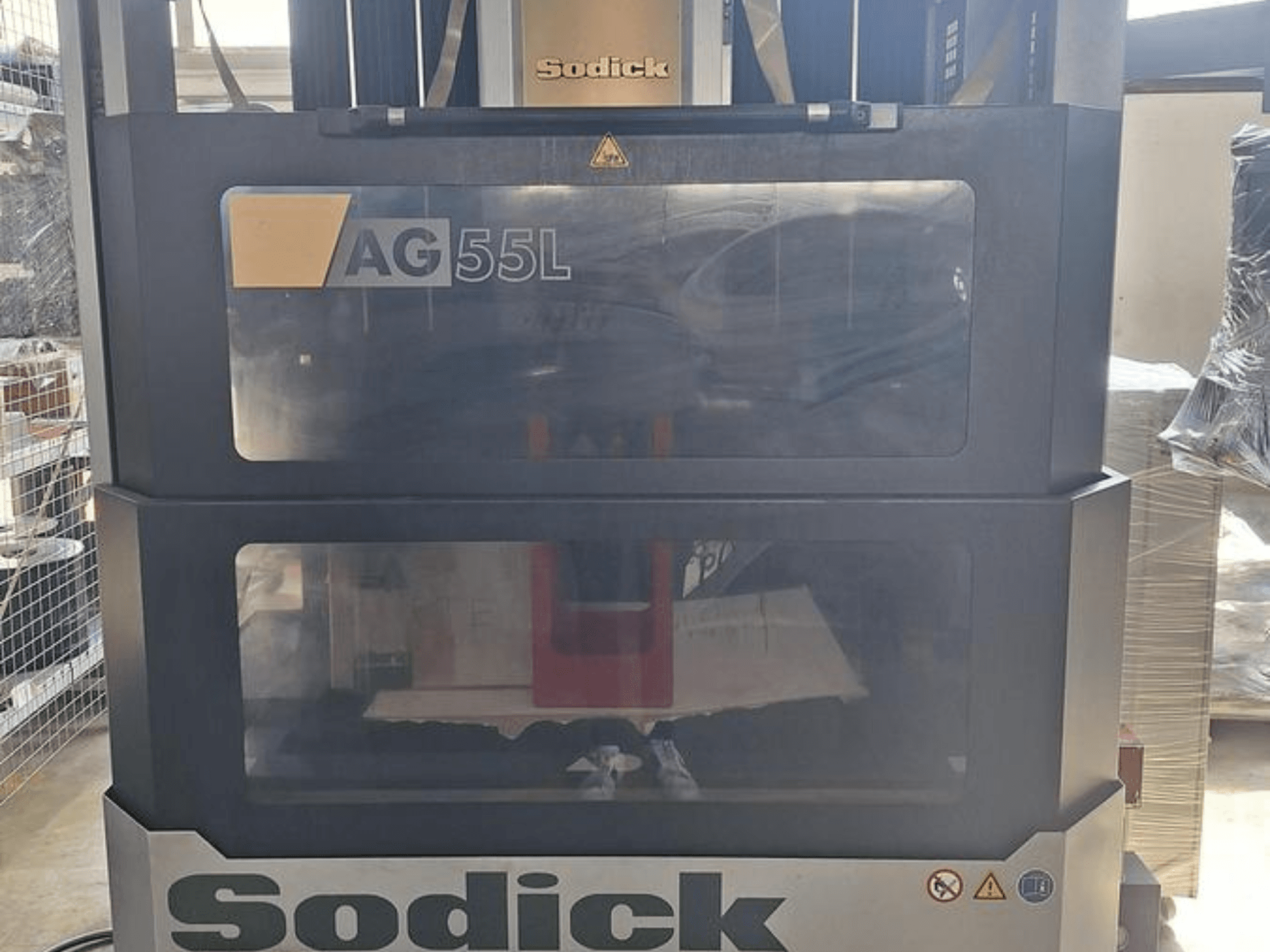 Електроерозійний прошивний верстат Sodick AG 55L, вид спереду з елементами керування, видимими крізь прозорі панелі, що демонструють робочий простір всередині.