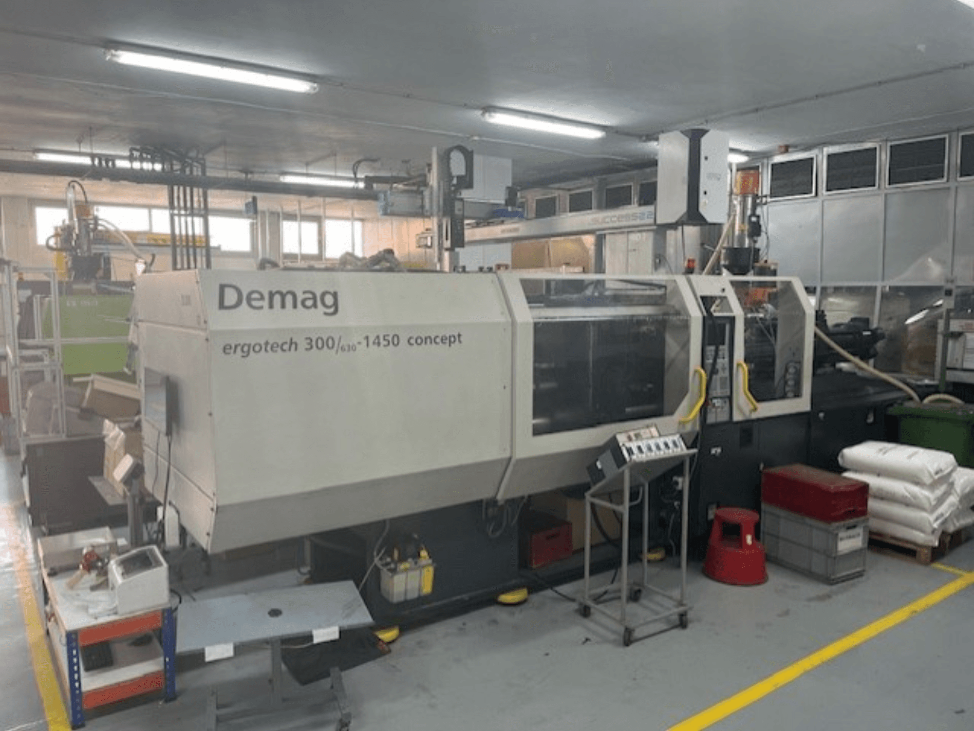 Гідравлічна машина для лиття під тиском Demag ERGOTECH CONCEPT 3000-1450, вид спереду, з елементами керування та матеріалами поруч.